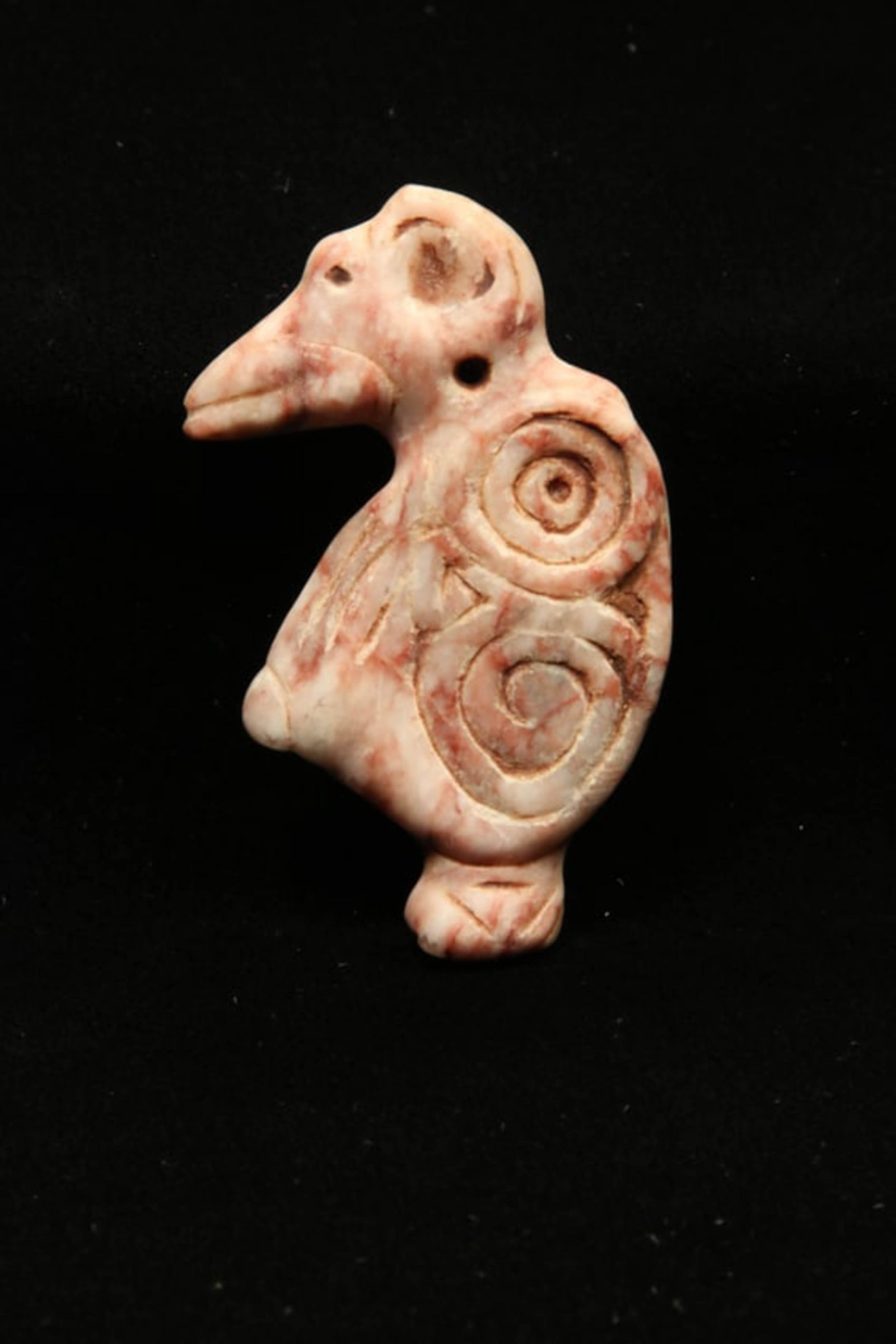 Pre-Columbian Bird Amulet: A cream and red stone Taino bird amulet with a long beak and circular designs on the wings. Suspension holes at neck. 2-1/2" H. Provenance: Ex collection Tony Milton, NM.