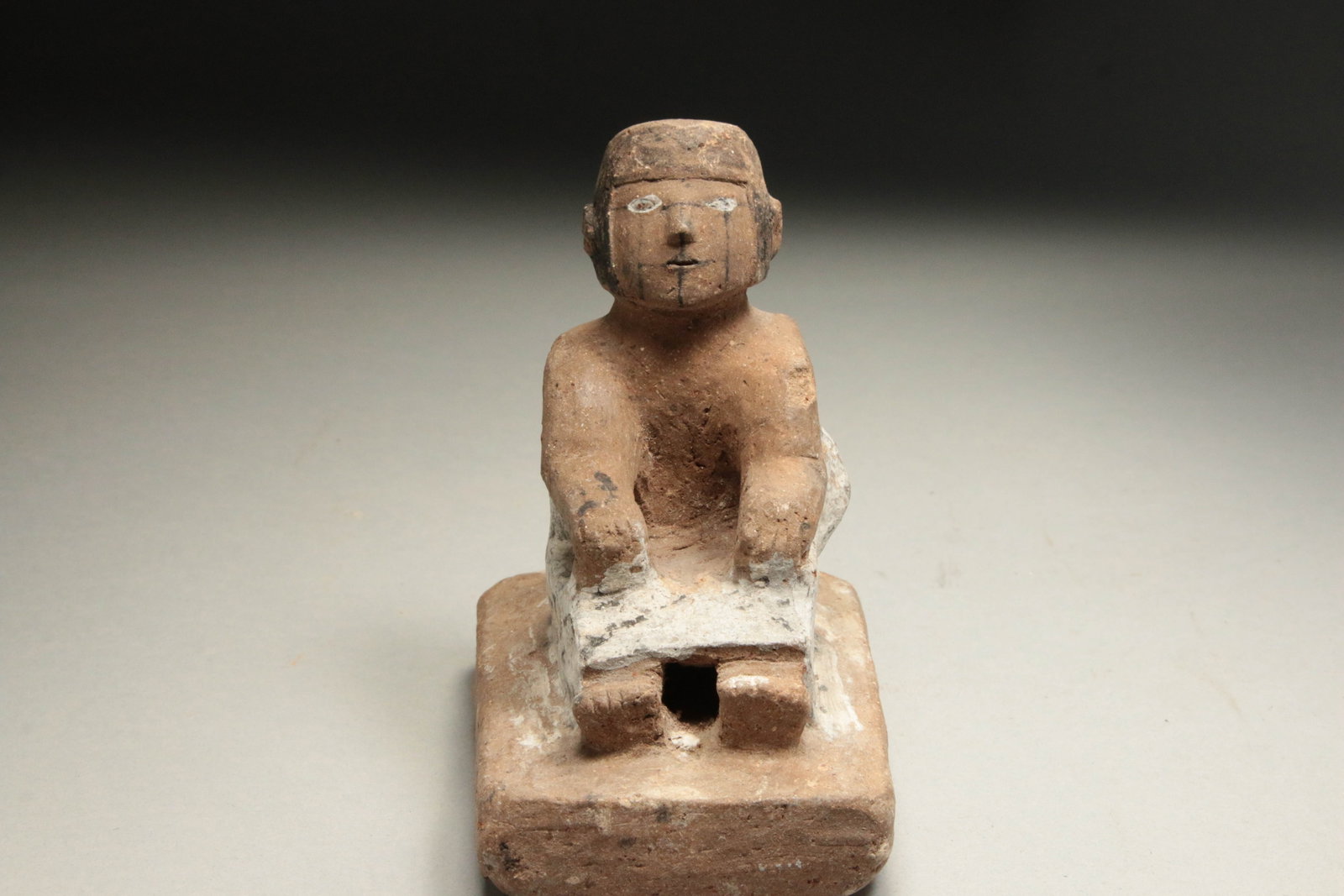 Pre-Columbian Narino Seated Figure: A ceramic female seated figure, Carchi-Narino, Columbia. Black and white organic pigments slips. 4"H. The sculpture depicts a stylized female figure seated firmly on a low stool or bench, which was tr