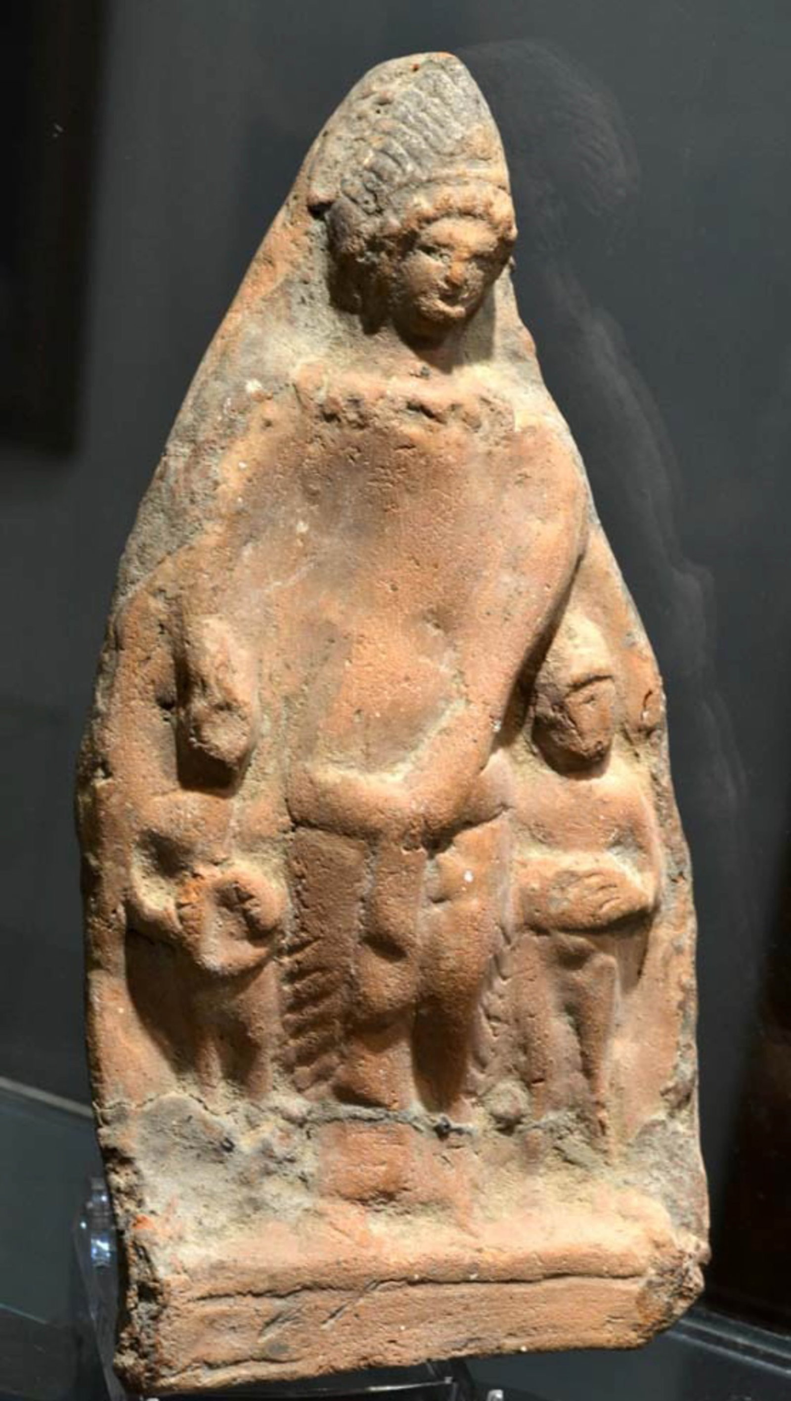 ANCIENT GREEK TERRACOTTA GROUP OF TELESPHORUS WITH CHILDREN: Terracotta group depicting a standing Telesphorus, depicting the healing god, possibly a son of Asclepius, flanked with 2 children, one on each side. Telesphorus is wearing the Celtic hooded coat.
