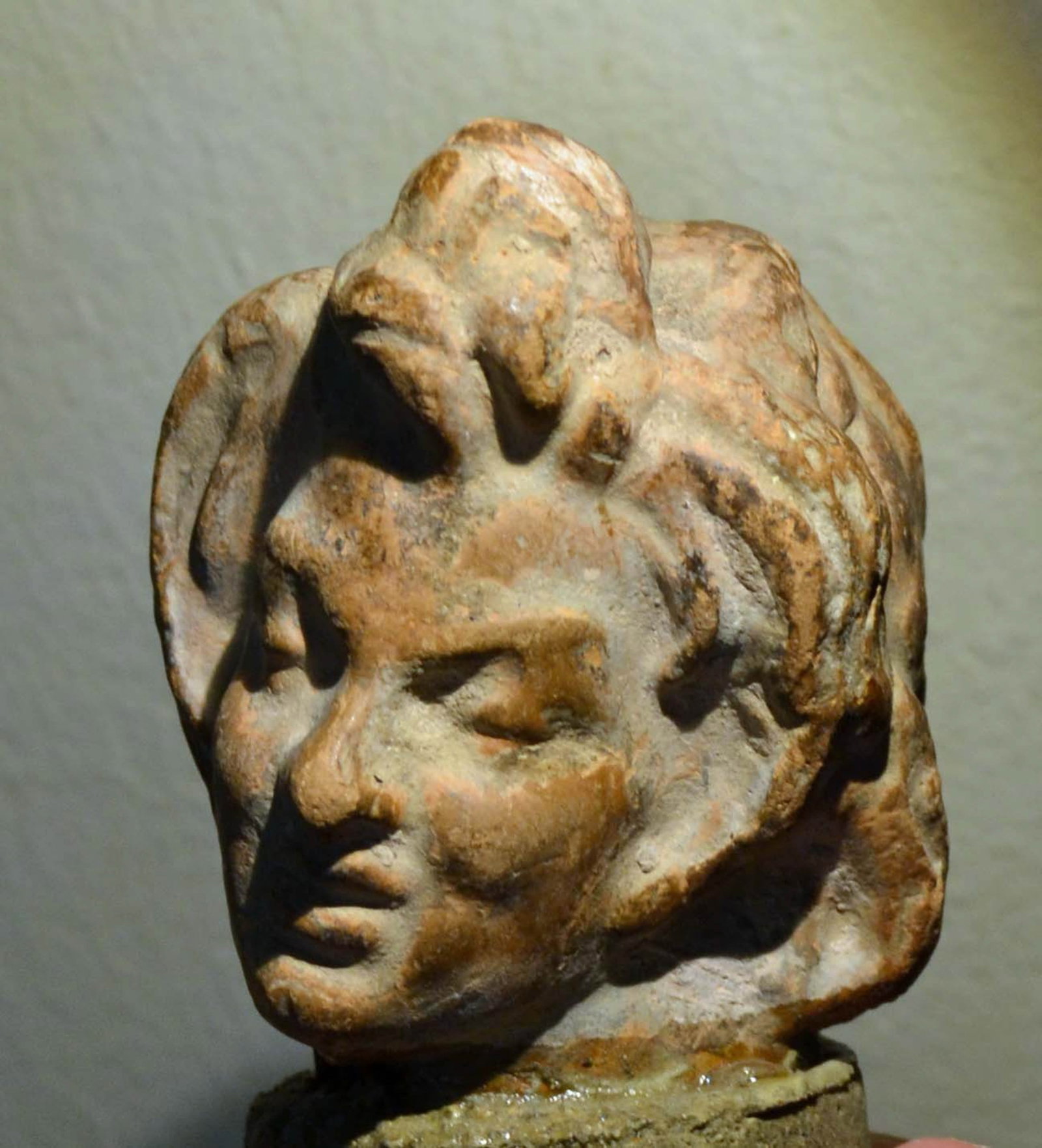 Ancient Greek Terracotta Head - 3rd Century BC: An ancient Greek Terracotta head of a young boy. With pleasant facial expression and with an elaborate hair style, 3rd Century BC. 2-1/4 inches high, With remains of original pigment. Provenance: EX p