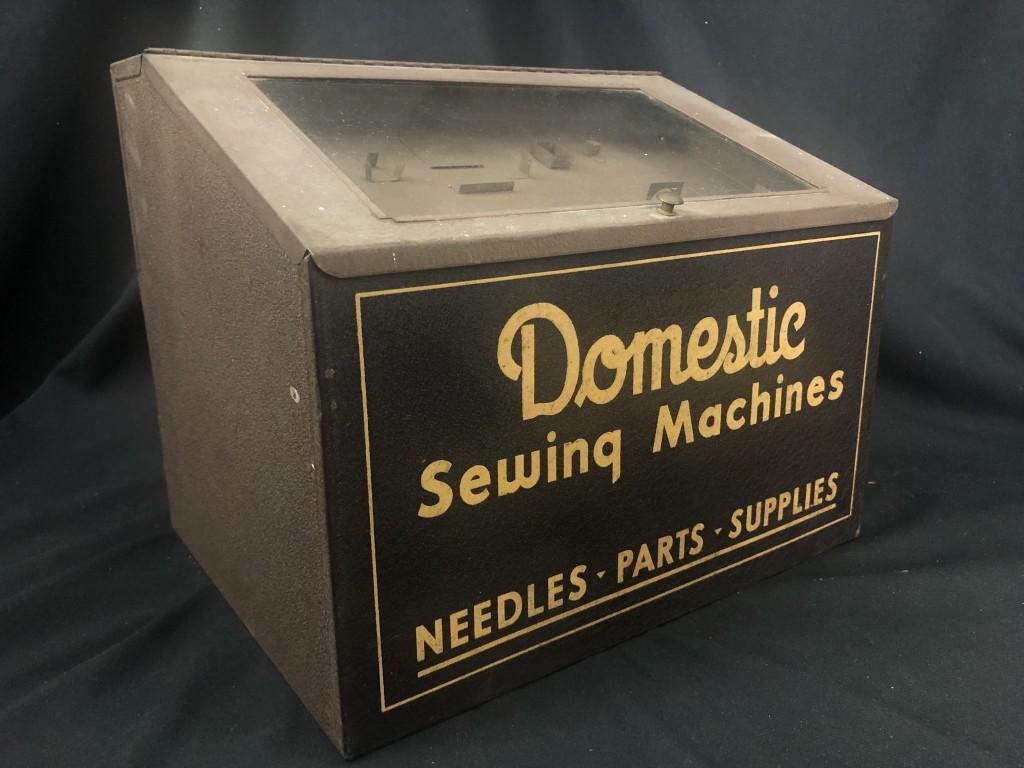 Domestic Sewing Machine Metal Cabinet w/ Items: Metal Store Display Cabinet with signage front "Domestic Sewing Machines, Needles, Parts, Supplies." Top opens up for display cabinet. Backside has three drawers with sewing parts. Measures: 13-3/4" w