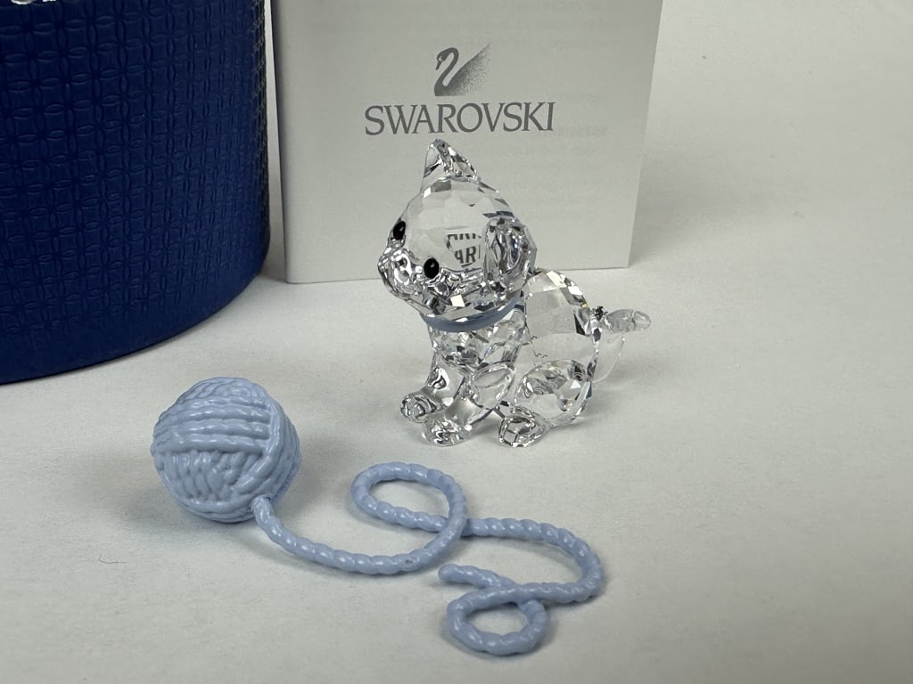 Swarovski Crystal Sitting Kitten w Yarn Ball w/Box: Swarovski Crystal Sitting Kitten w Yarn Ball w/Box Cut crystal figurine of a sitting kitten with a light blue color and matching metal ball of yarn made by Swarovski of Austria. In original box. Measu