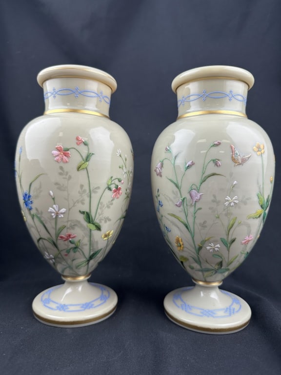 Pr. Handpainted Opaline Glass c.1800 Floral Vases: Pair of antique urn shaped pedestal opaline buff glass vases with delicate raised handpainted flowers and butterflies over foliage silhouette background with gilt accents and blue enamel design. Victo