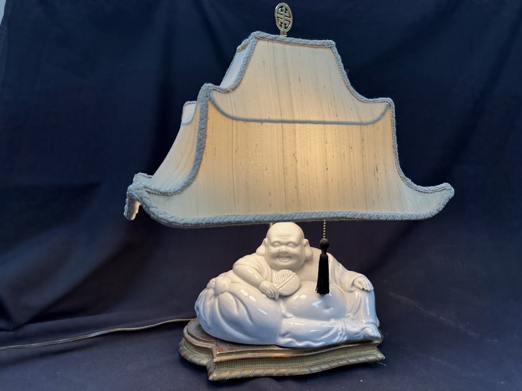 Laughing Buddha Porcelain Figural Accent Lamp: Porcelain laughing Buddha, or Budai, figure accent lamp on custom gold wood podium topped with pagoda shaped lamp shade over double bulbs. Seated Buddha figure with fan is sure to bring good fortune.