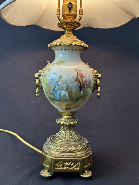 French Brass & Porcelain Urn Lamp 1 of 2: An antique French style porcelain table lamp with brass mount. Handpainted figural scene on one side and a landscape on the other, accented by lions head handles. Measurements: Body: 14" H x 5" W Shad