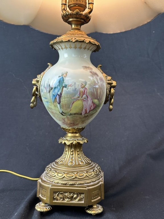 French Brass & Porcelain Urn Lamp 2 of 2: An antique French style porcelain lamp with brass mount. Handpainted figural scene on one side and a landscape on the other, accented by lions head handles. Measurements: Body: 14" H x 5" W Shade: 11-