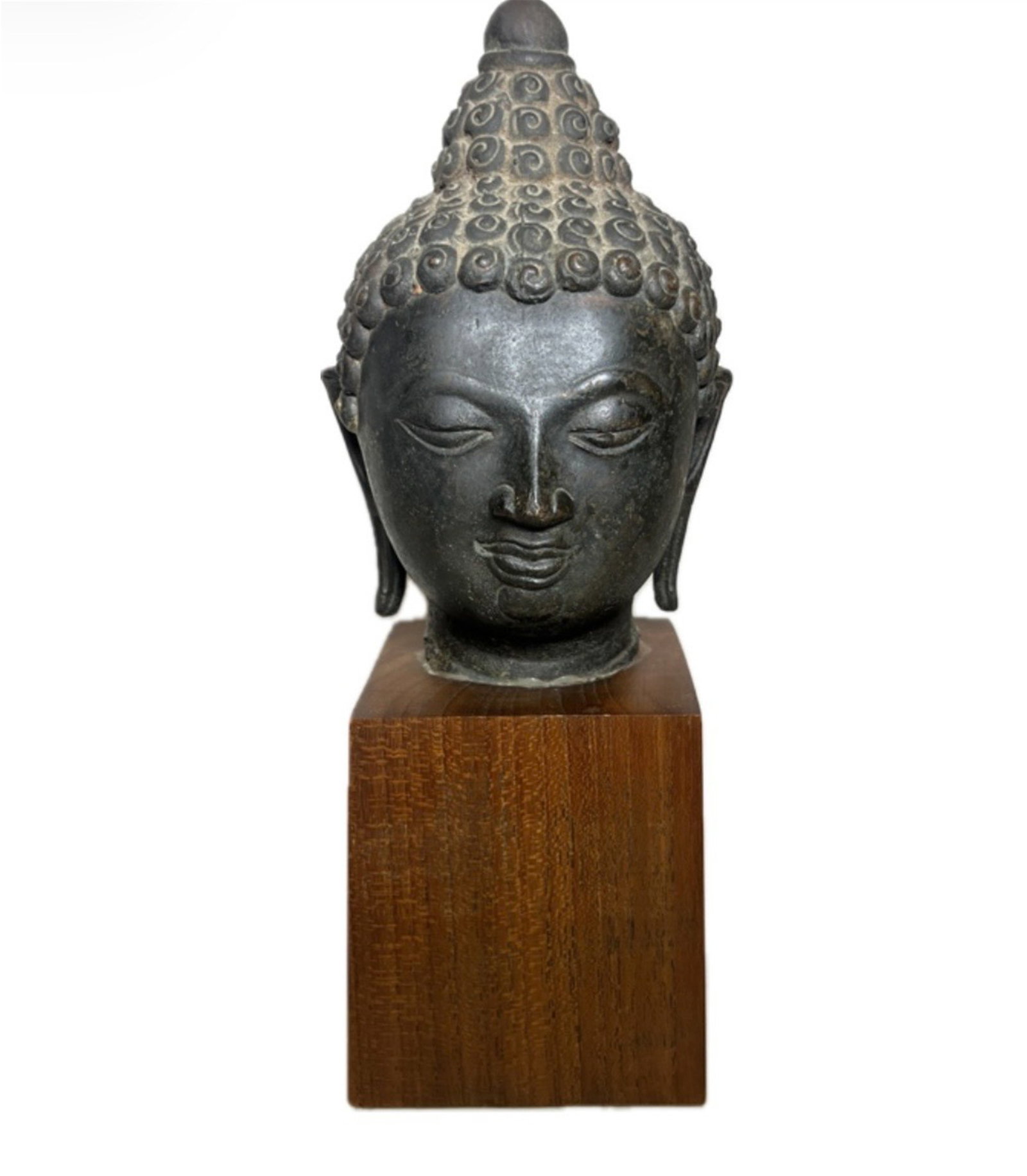 A BRONZE BUDDHA HEAD: A BRONZE BUDDHA HEAD The face with downcast expression, incised eyebrows and eyes, smiling lips, aquiline nose, elongated earlobes, high chignon, with surface oxidize marks. DIMENSION: H. 26 cm.?with