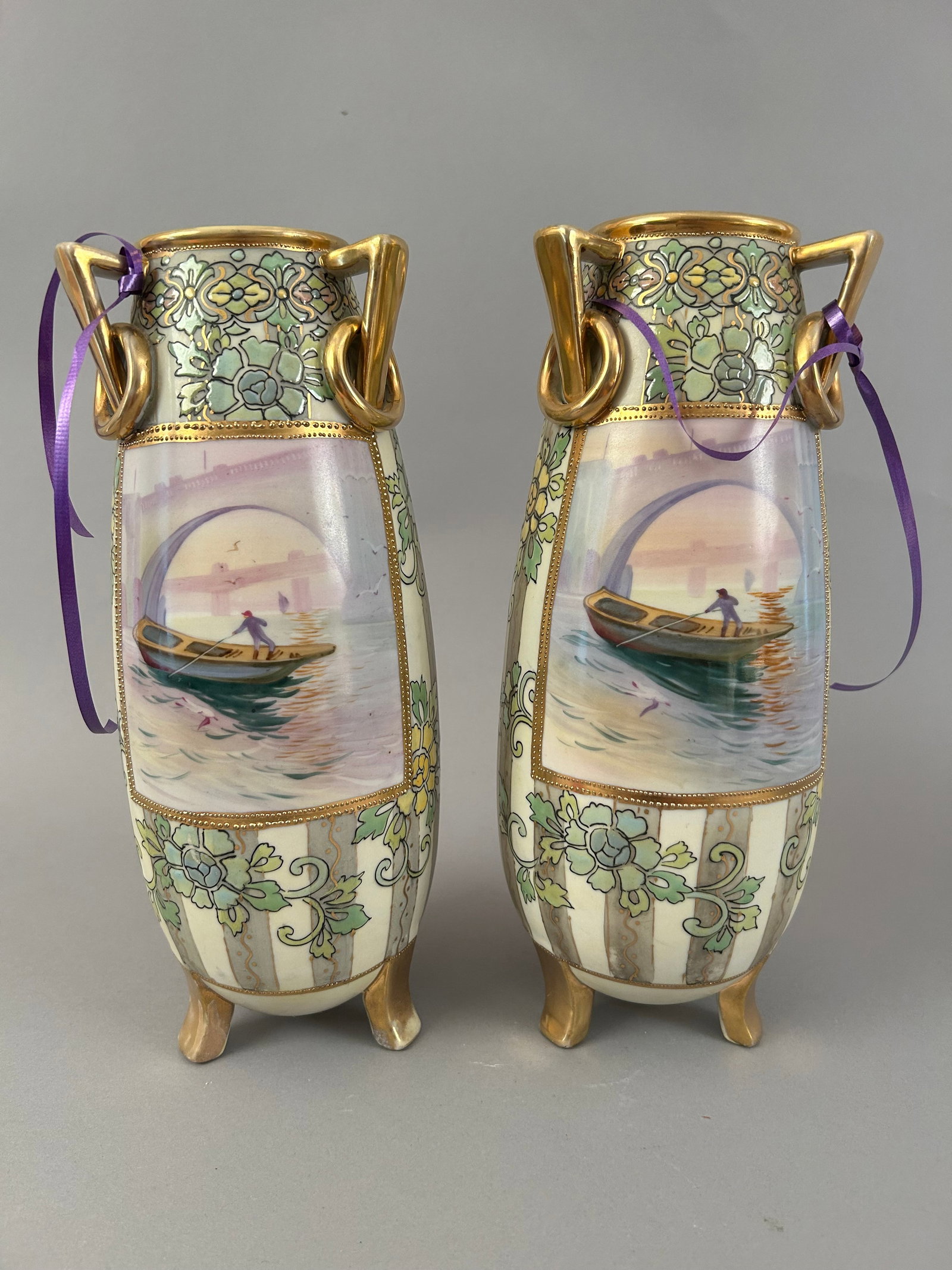 Pair Of Tri Footed Three Handled Vases With Boating Scenes: Pair of three toed three handled vases with boating scenes and some raised detail. Gold gilt embellishments. Unmarked but likely Nippon.