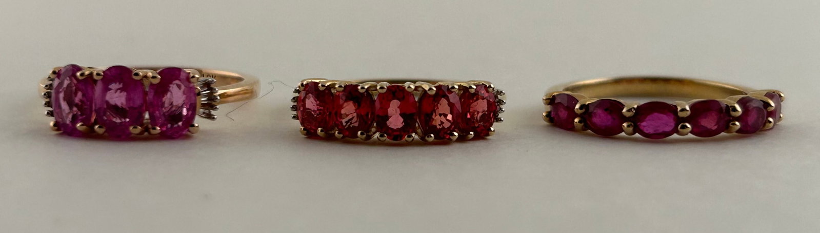 Three 10 Karat Gold Rings, Two With Diamond Accents.: Three 10 Karat Gold rings. Two with pink sapphires and one with orange stones possibly garnet or topaz. Two with small diamonds. Two Size 6 and 1 a little smaller.