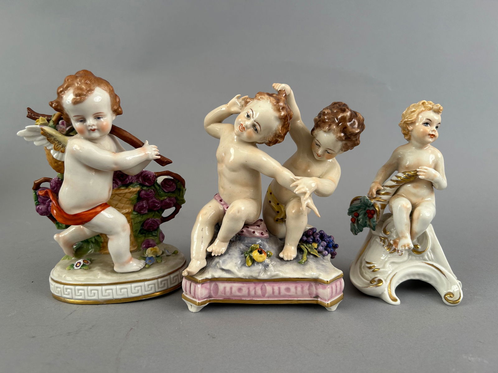 Three Small Porcelain Cherub Figurines: Three small porcelain cherub figurines. Two marked on the bottom. One is a small vase or toothpick holder.