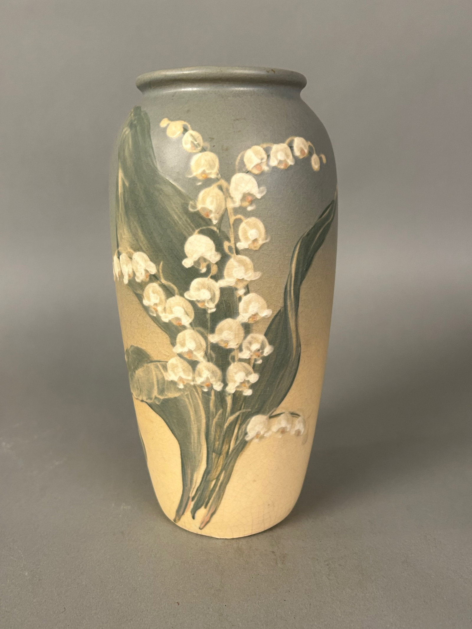 Art pottery vase, early 20th century, lily-of-the-valley: Art pottery vase, early 20th century, 6.5 in. high. Cylindrical form with hand-painted lily-of-the-valley decoration on a crackle-glazed gray-to-cream ground, signed “England” to lower body. 9