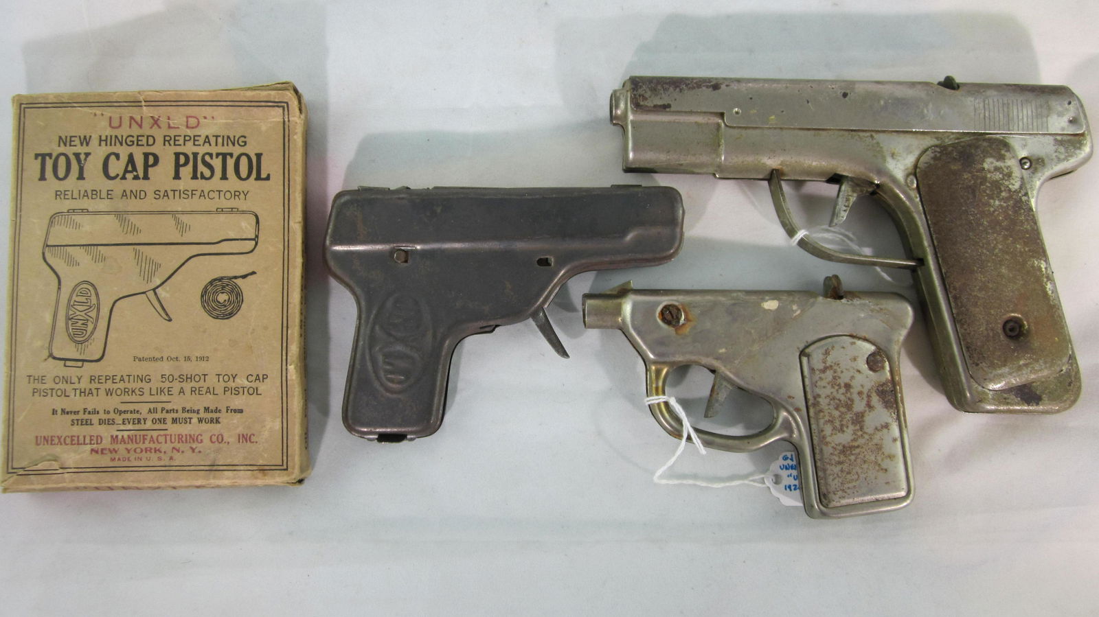 UNXLD Pressed Steel Cap Gun Assortment.: Unexcelled Co. repeater cap pistols in pressed steel, "45" is 6 1/2" long, a non-working "Scout "clicker gun dated 1914, 4 1/2" long in pressed steel painted black, another gun with patent date 1912 i