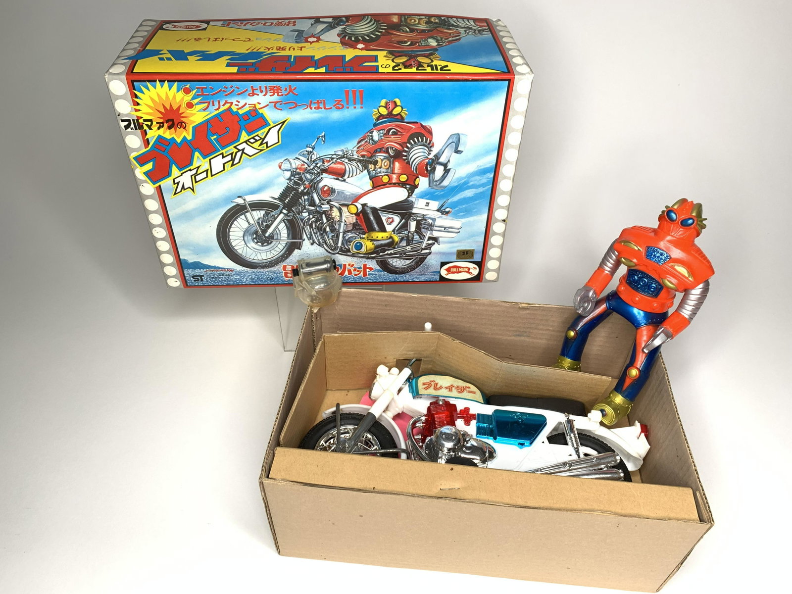 Bullmark Friction Buraizer (Blazer) Motorcycle: Made by Bullmark. Japan. Hard plastic and tin. Measures 10 1/2 inches in length. Retains original helmet and cardboard inserts. With original box for Japanese market. Condition Figure Excellent. Condi