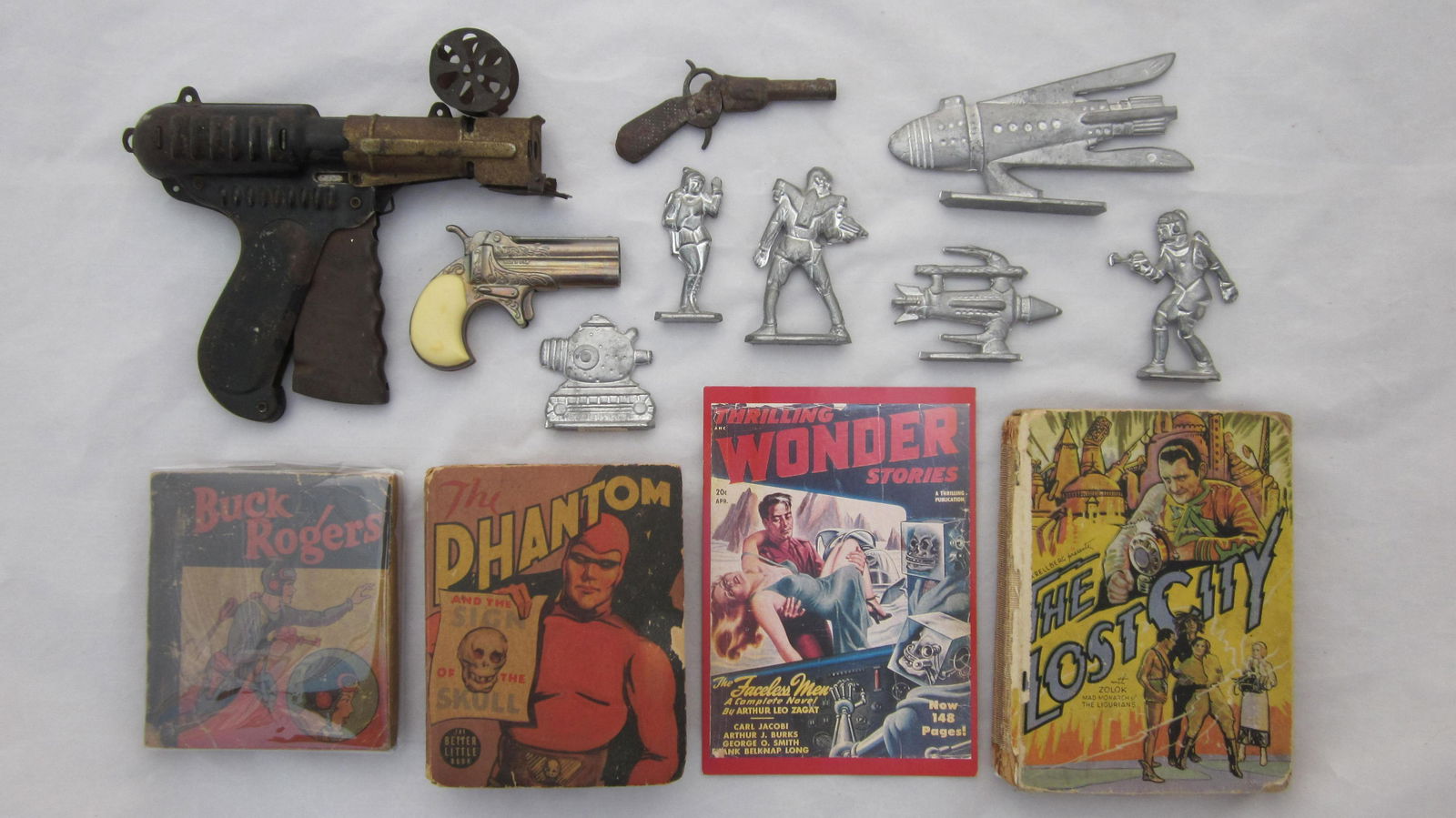 Cap Gun And Space Figure Assortment: NuMatic Cap roll cap gun (dated 1936), small tinplate single shot cap gun circa 1880, Derringer cap gun circa 1960, Buck Rogers book circa 1937, "Phantom" book dated 1939, promotional book "The Lost C