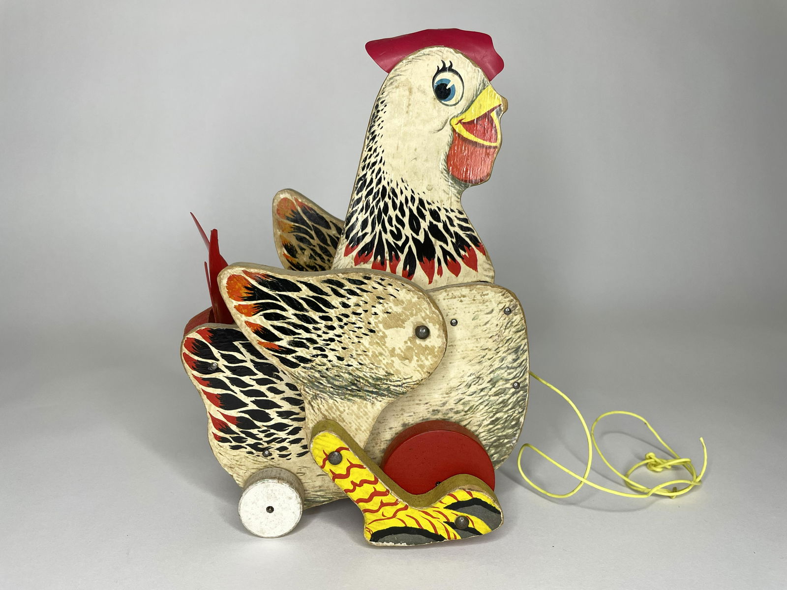 The Crackling Hen Pull Toy: Cracking Hen #120. Made by Fisher Price. Circa 1960s. 6 1/2 inches long by 9 1/2 inches high. Paper litho on wood. Fine Condition. Some paper loss to left side of hen.