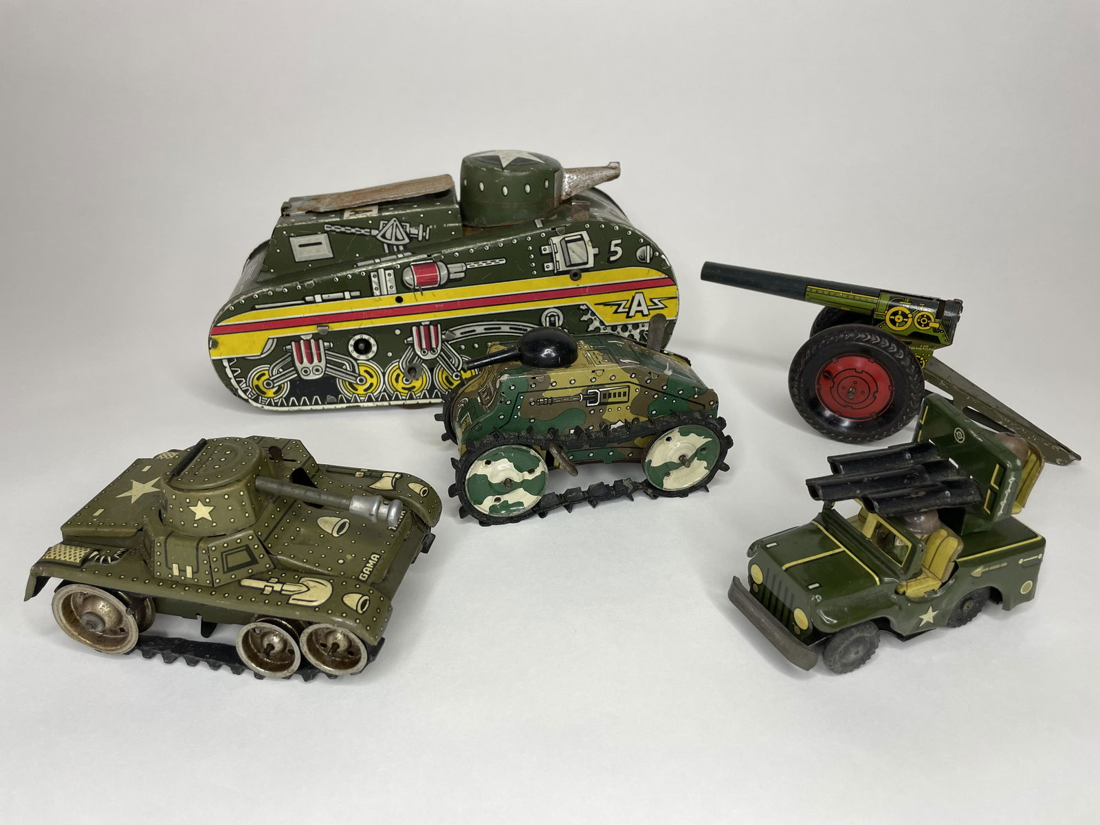 Lot of Wind-up Tanks: Including Marx A5, 10 inches long, missing man and replaced cover. Marx WWI Wind-up Tank, 5 1/4 inches long. Gama Tank, 5 inches long. Anti-Aircraft Jeep, 4 1/2 inches long. Field Gun, 8 1/2 inches, n