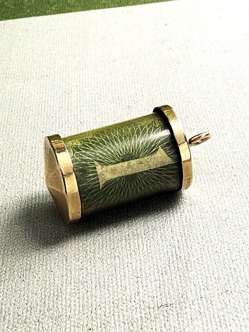 A Vintage Cylindrical Charm With A One Pound Banknote, Mount Hallmarked 9ct London: A Vintage Cylindrical Charm With A One Pound Banknote, Mount Hallmarked 9ct London, approximate gross weight 5.5 grams.