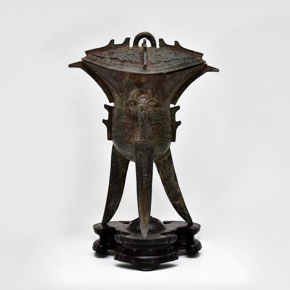 An archaic ritual bronze covered wine vessel,jue: The Chinese antique ritual bronze covered wine vessel cast with a deep 'U'-shaped body supported on three blade-form legs, finely cast in low relief to the center with a band of archaic Kui dragon mot