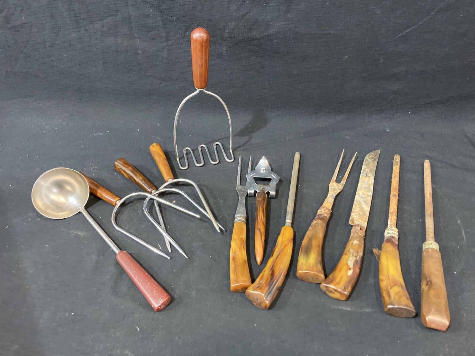 BAKELITE UTENSILS: INCLUDES MASHERS, LADLE, MEAT FORKS, KNIVES AND SHARPENER A FEW PIECES IN THIS LOT SHOW SURFACE RUST ON BLADES