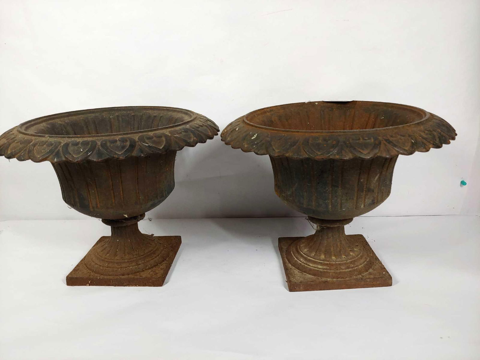 DECORATIVE CAST IRON URNS: EACH IS ORNATE, DECORATED WITH A HEART PATTERN AROUND RIM. 12 IN TALL X 16 IN DIAMETER. A HOLE IN EACH CENTER FOR PROPER DRAINAGE. SOME MINOR SURFACE RUSTING SHOWS THROUGH OLDER PAINT.