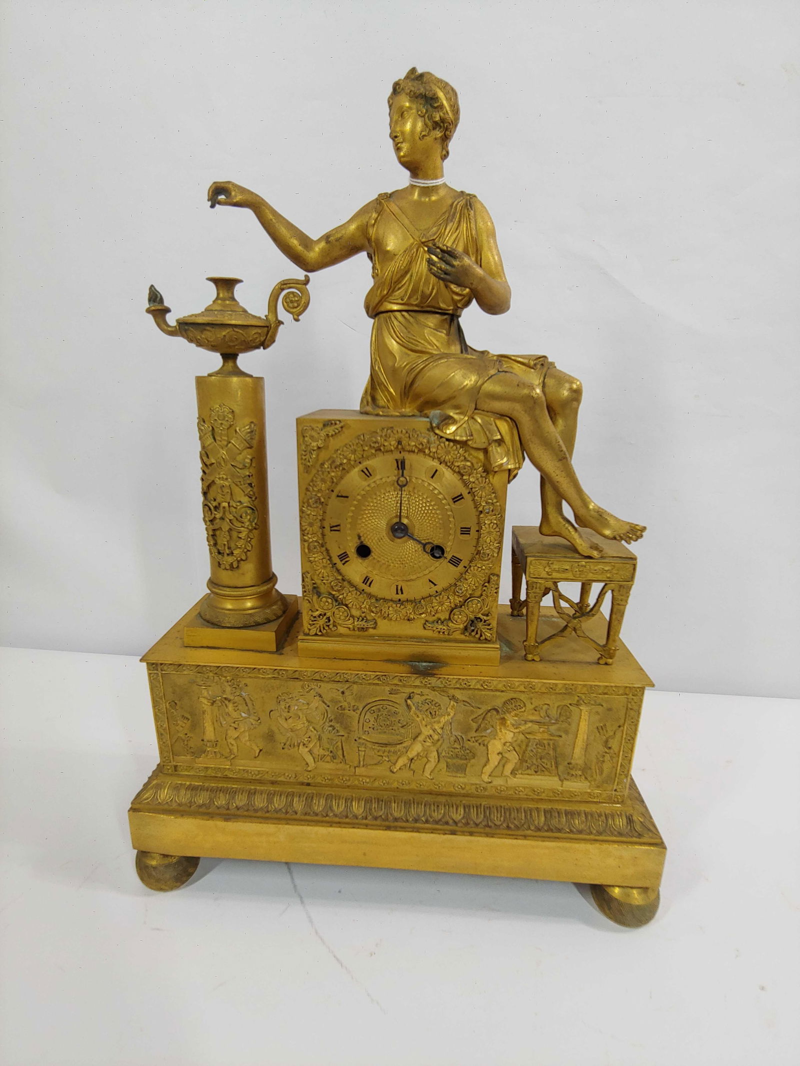 EMPIRE GILT BRONZE PENDULUM CLOCK: KEY WIND, FEATURING ROMAN FIGURE ATOP CLOCK WITH STOOL AND DECORATED URN. CHERUBS DETAIL LINE LOWER HALF OF CLOCK. PENDULUM AND KEY ARE NOT PRESENT. 12.5X 18X 5