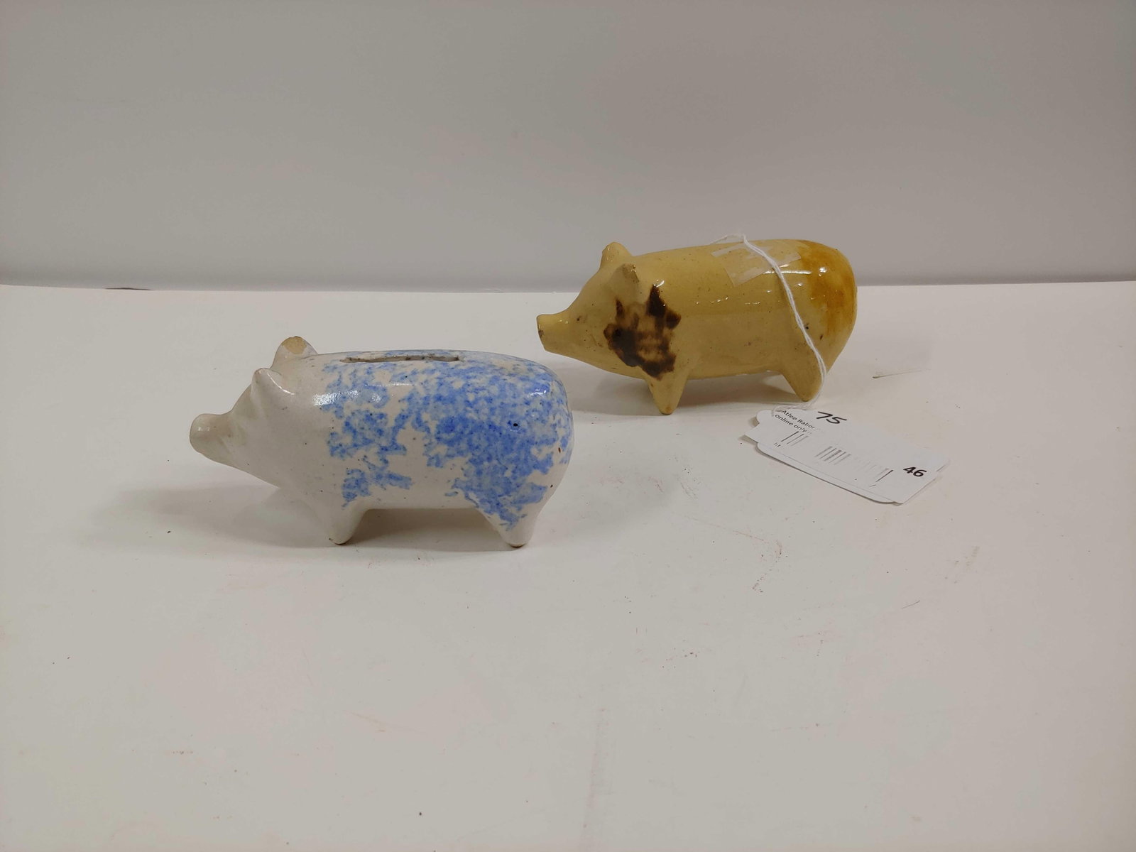 STONEWARE PIGGIES: ONE IS A COIN BANK, OTHER HAS A HOLE FOR UNKNOWN PURPOSES ON BACK END. EACH IS 5 IN LONG