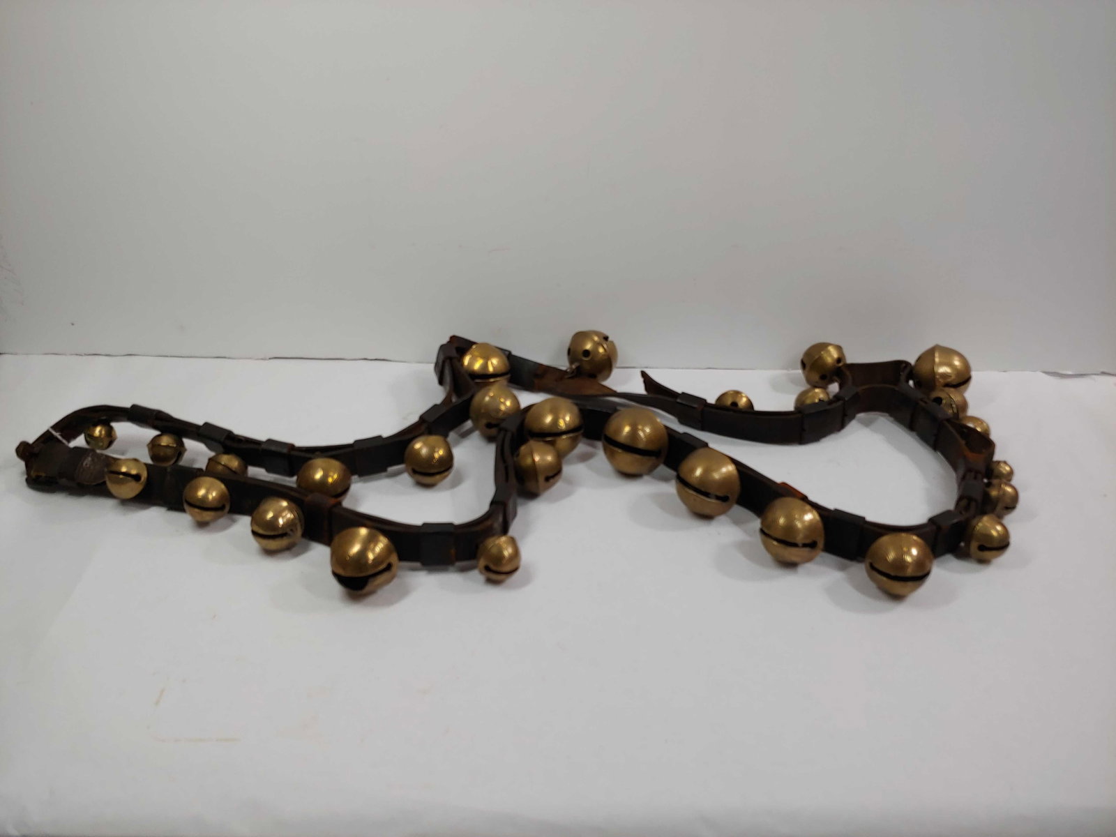 Strand of 28 brass graduated sleigh bells on leather belt: A few bells are cracked and leather belt shows condition in areas, also has 1 unfastened bells, but overall is a desirable strand.