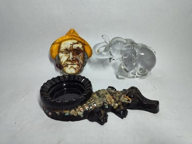 Cast iron fisherman ashtray, resin alligator ashtray and glass figural elephant