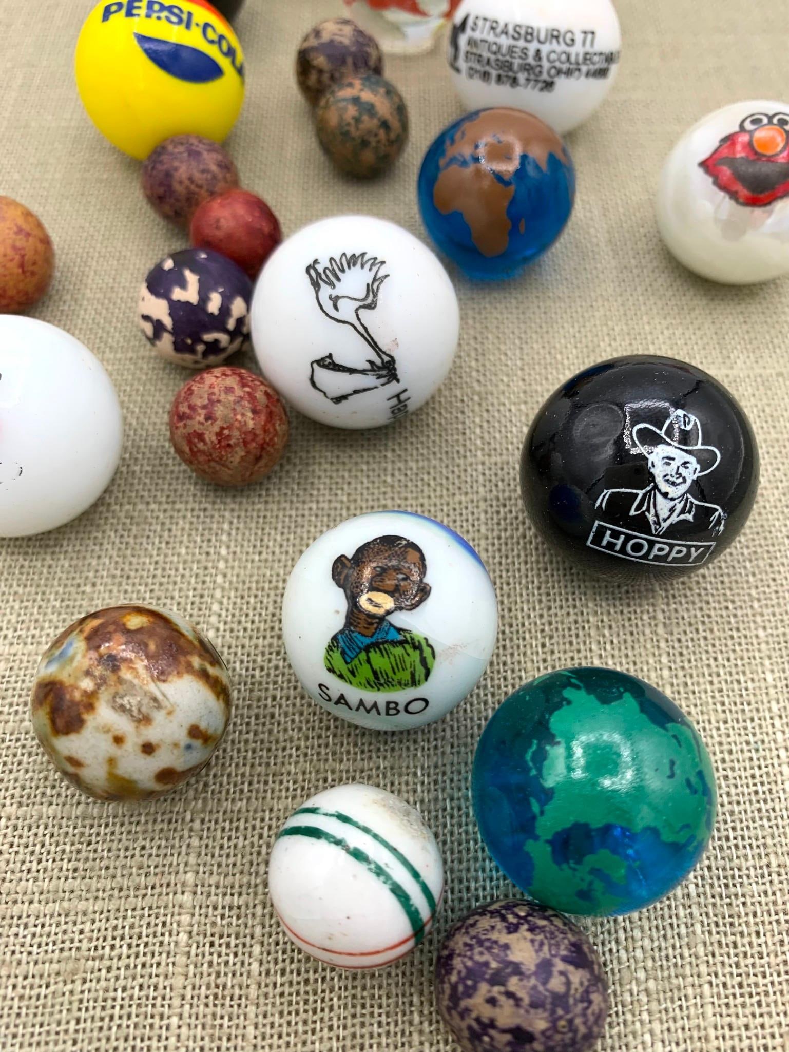 24 Vintage Sambo, Mickey Mouse, Hoppy, Pepsi Cola, Glass Shooters and Early China, Clay, Marbles: 1" to 1/2" in size, one early hand painted china marble, assorted clay and pottery marbles along with larger advertising shooters.