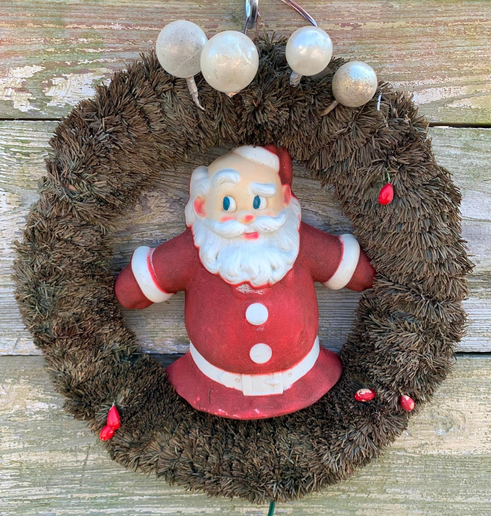 Mid Century Flocked Santa Claus Light Up Wreath Holiday Decoration: 15" x 13", early cord, needs a fresh bulb, flocked plastic and metal Santa light, mercury glass ball and berry detailing, some shedding to the wreath material.