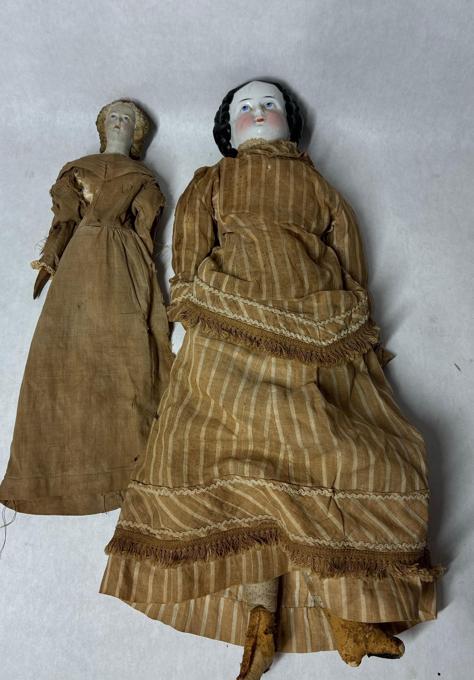 Early Bonnet Head & Bisque Head Dolls: Larger doll features a fabric body with leather shoes. Stuffed with horsehair, no hands, no marking to head. 18 inches tall. Other doll with bisque head, leather body, and wood limbs. 13 inches tall.