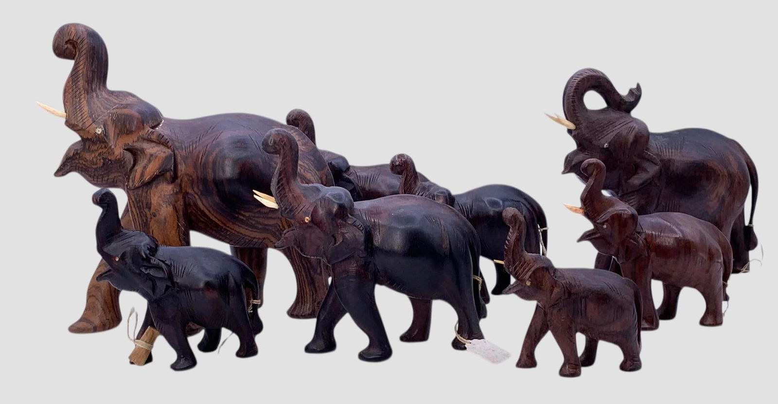 Family of 8 Vintage Hand Carved Rosewood Raised Trunk Good Luck Wooden Elephant Statues: Old India tags on 7, ranging in size from 8" tall to 3 5/8", two have their tusks wrapped in paper around a leg, the smallest is missing a tusk, one front foot on a 4" elephant has damage as shown, be