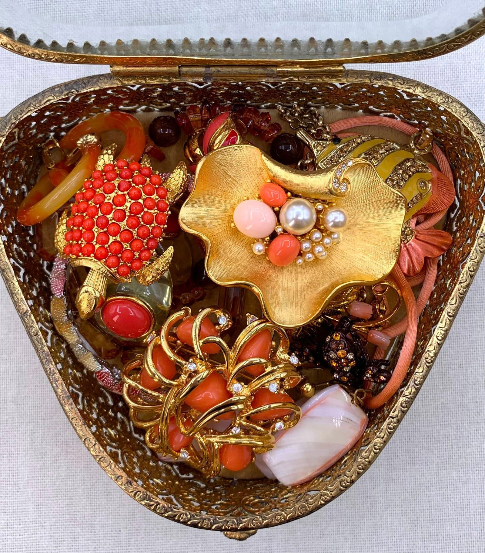 19 pc Mid Century Pierced Metal Jewel Casket Full of Vintage Jewelery: Ivana, Joan Rivers, Trifari, glittering rhinestones, faux pearls, coral hued baubles, Glittering winged Bee, Tortoise and Clam Shell tucked into the velveteen lined pierced metal jewel casket, hinged