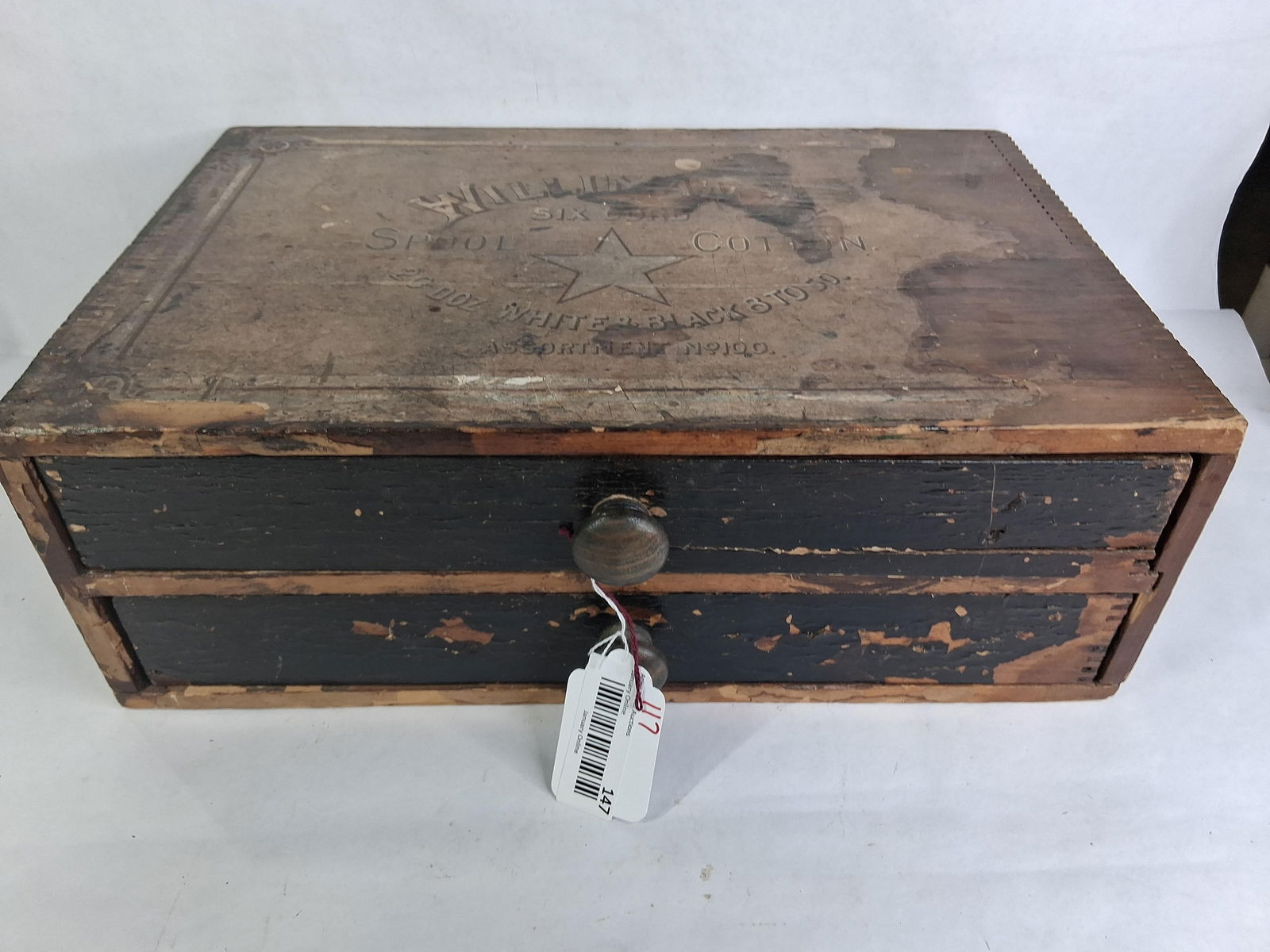Willimantic Spool Cabinet: Two drawer cabinet, dovetailed corners and drawers. Original paper label shows to top but is peeling in areas. One side and drawer fronts have been painted black. Back side shows a great label.