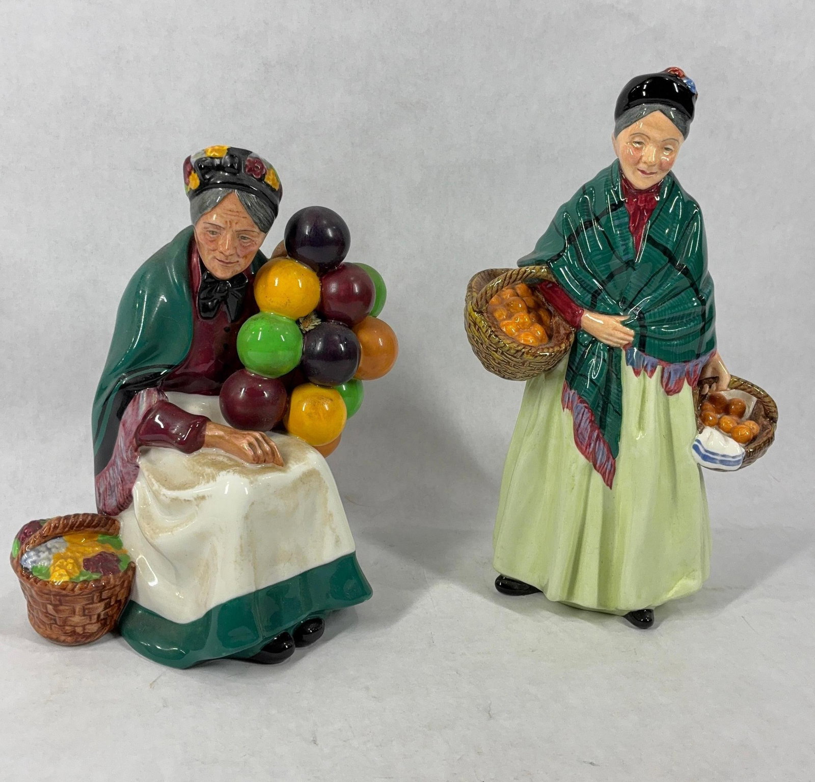 Royal Doulton Lady Figurines: Featuring the Orange Lady and the Balloon Seller. Orange lady is signed and dated 1953, 8 inches tall. Balloon seller is seated and 7.5 inches. Both in good condition.