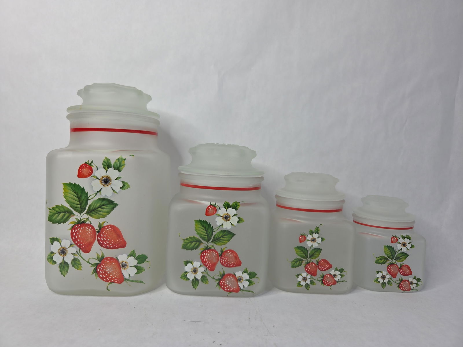 West Moreland NOS Frosted Strawberry Canister Set: Frosted glass canisters and lids with airtight plastic seal insert. Large canister has a small stain on lid. Otherwise in good condition. 9?in tall, 6?in tall, 5?in tall, 4?in tall new old stock in or
