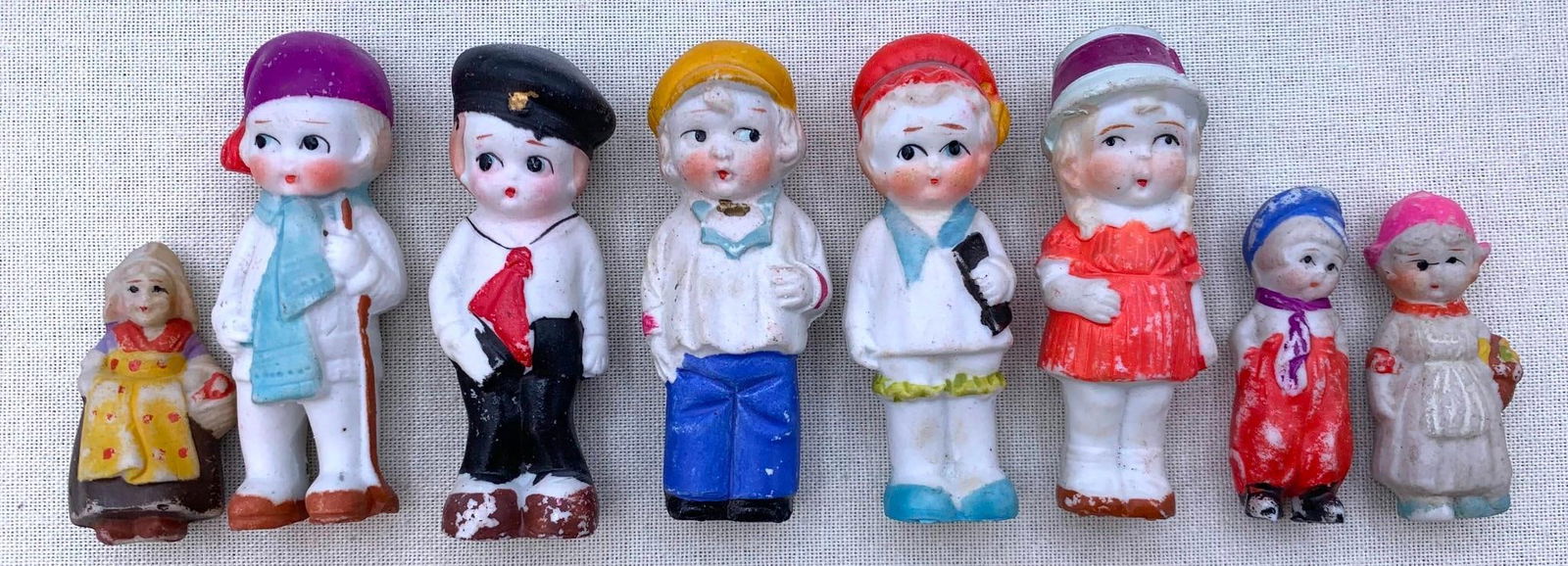 Eight 1920s JAPAN Bisque Arcade Penny Dolls: JAPAN marks on most, each approx. 3 3/8" to 2 1/2", hand painted in vibrant colors.