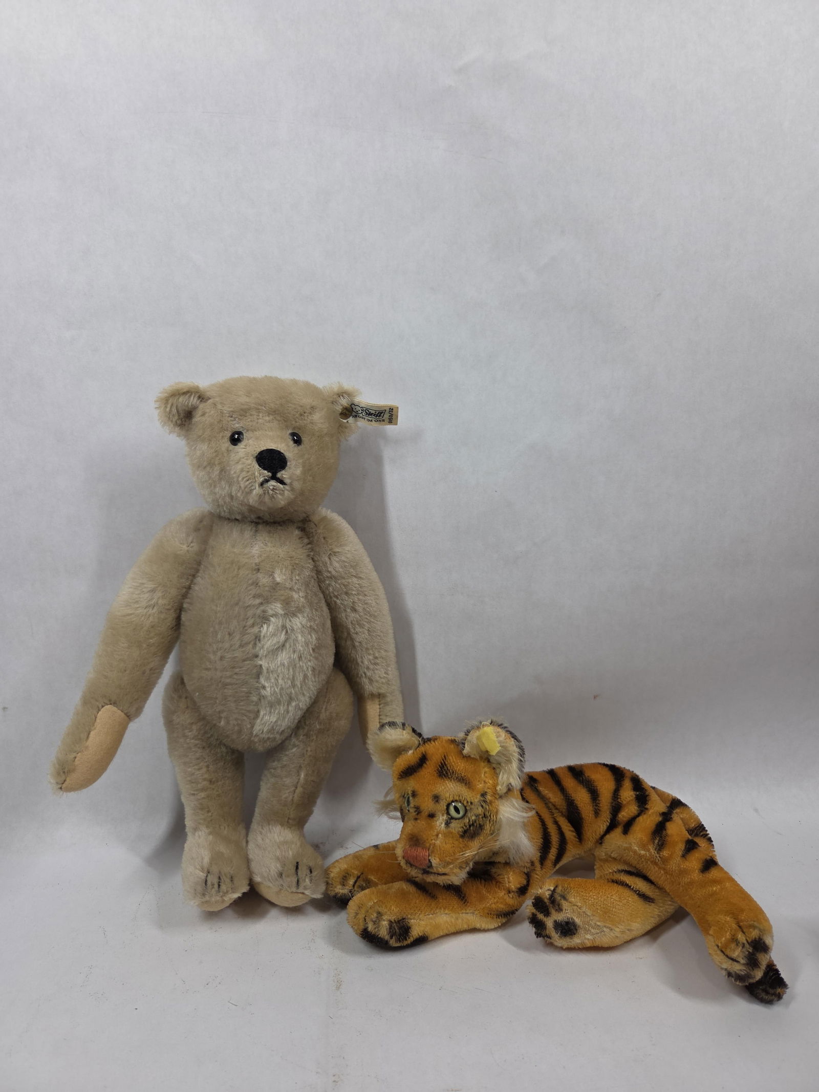 MoHair Steiff Floppy Tiger and Teddy Bear: Bear tag number 0150/32 with articulated arms. 11 inches long. Tiger is in lying position, tag is worn but present. 8.5 inches.