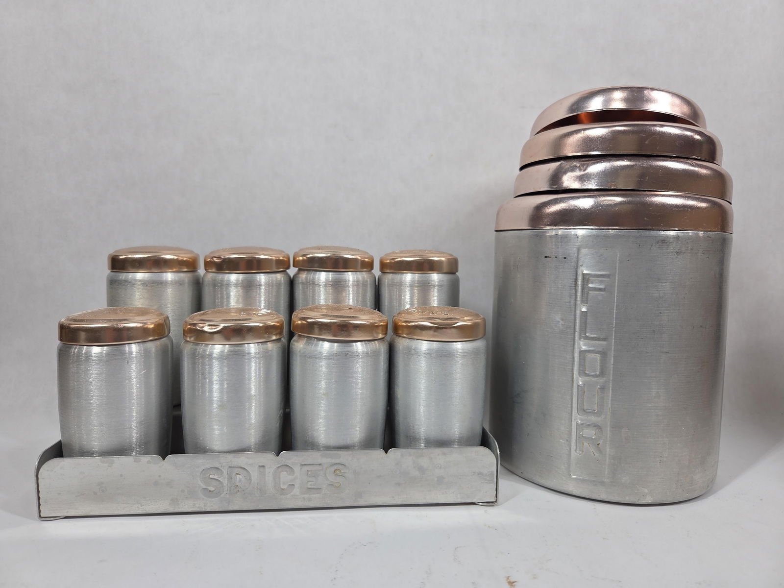 1950s Aluminum Canister & Spice Set: 4 vintage canisters with lids, and 8 spice jars with holder. Several dings show but all are complete and display well.