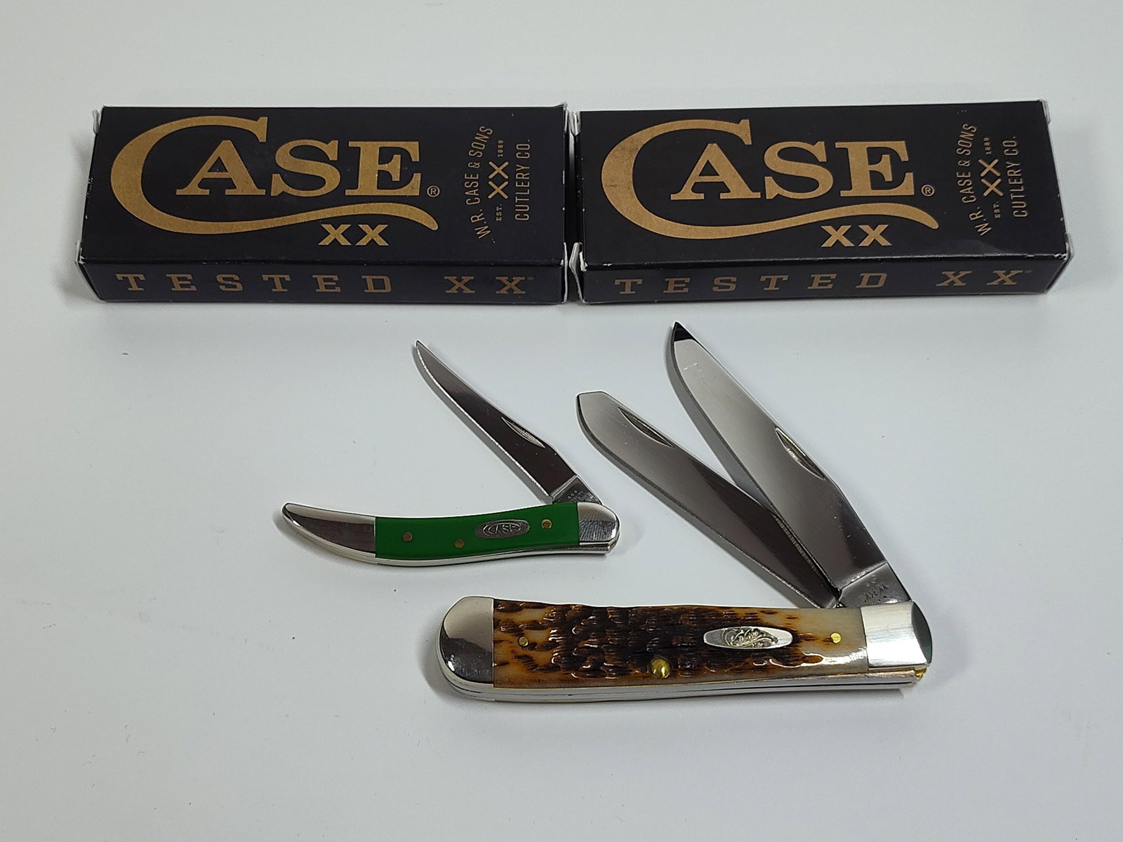 Case XX Pocket Knives: Amber Bone Peach Seed Jig Trapper and Green Synthetic Smooth small Texas toothpick. Both with box.