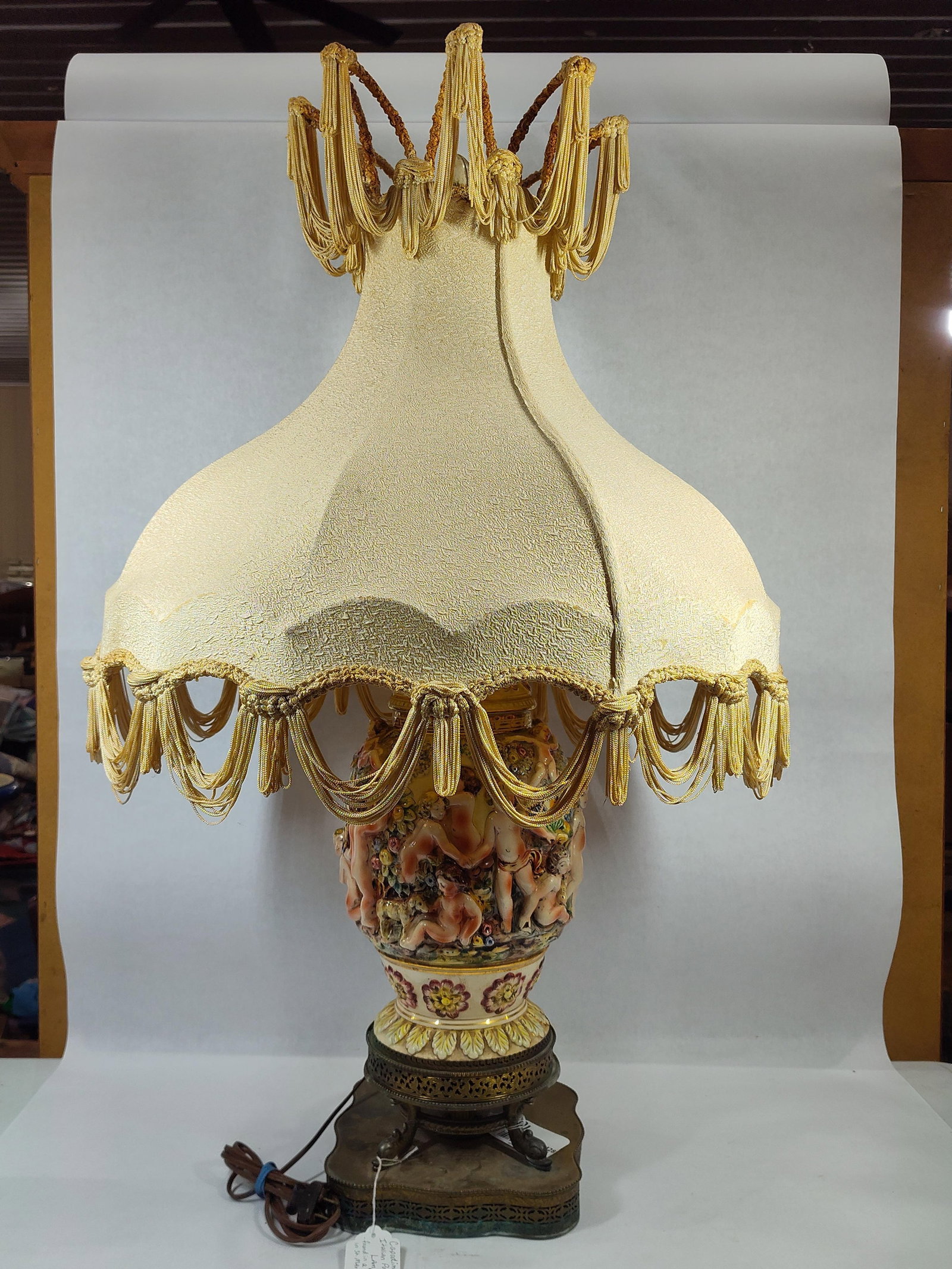 VTG Italian Capodimonte Style Intricate Porcelain Reliefs of Cherubs and Floral Rococo Scene Lamp: Original shade with brass/copper base showing tarnishing and minor condition issues as shown in photos with no chips,cracks or breaks in good working order standing 37 in H to top of finial