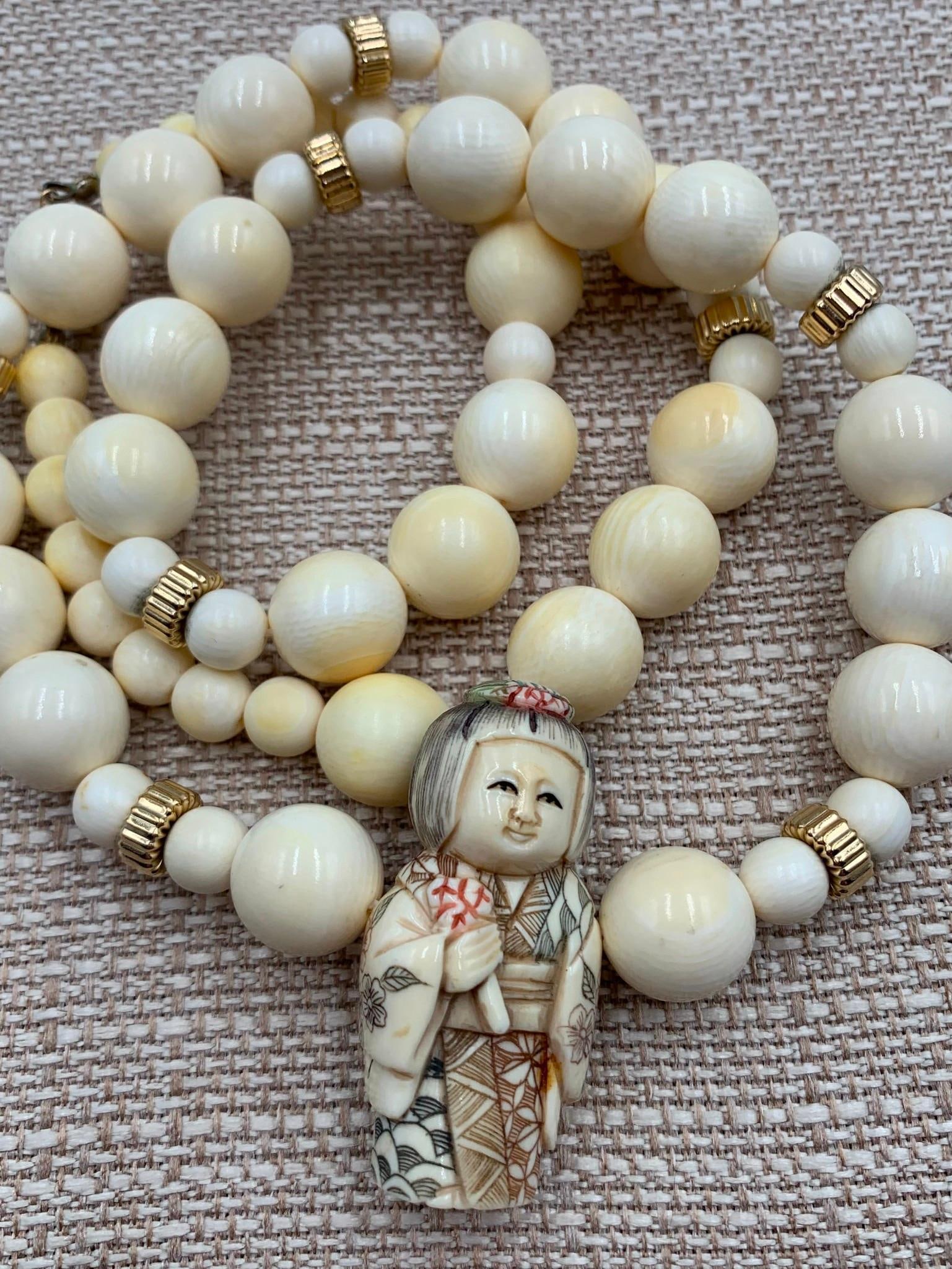 10k Gold Bead, Hand Carved Artist Signed Japanese Geisha Netsuke Natural Bead Necklace: 14k hallmarked clasp, 10k tested gold beads, graduated polished natural material beads and hand carved 1 3/4 IN x 7/8 IN netsuke, artist signed, 28 IN length.