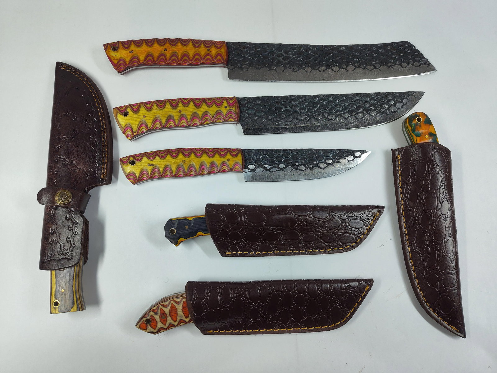 Damascus Hand Forged Carbon Steel Fixed Blade Knife Lot w/ Multi Colored Wood Handles and Leather Sh: Blades range in length from 4 to 9 in. with leather sheathes and multi colored wood grain handles