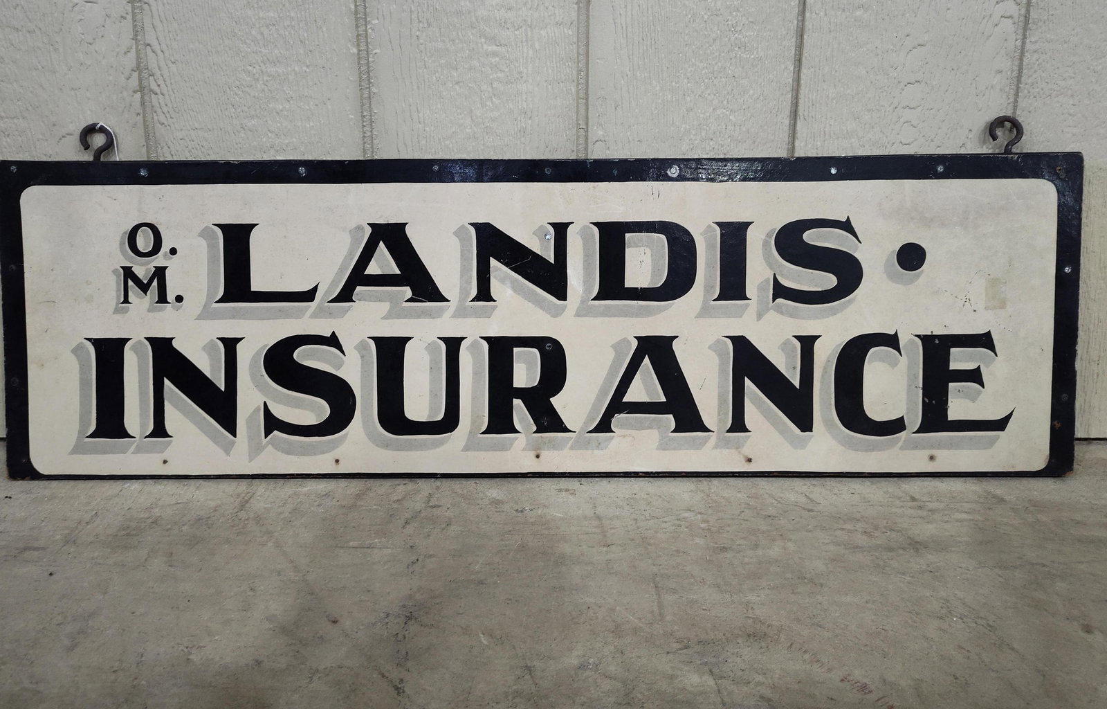 O.M. Landis Insurance masonite sign: 1-sided painted masonite sign on wood frame with hangers. 11.5in x 39.5in.