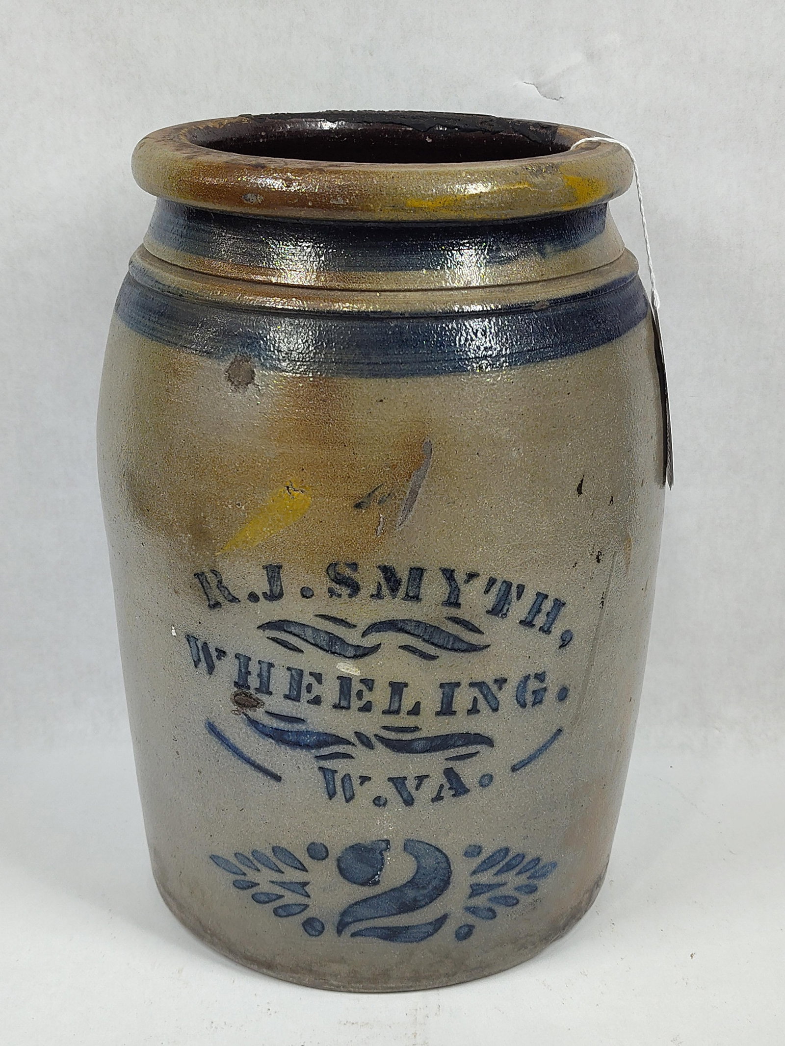 R.J. Smythe 2-gal stoneware jar: Wheeling, WV. Shows a chip on rim and a faintly visible hairline on left side (hardly noticeable). Also shows a few firing blemishes but has a great look!! 12in tall.