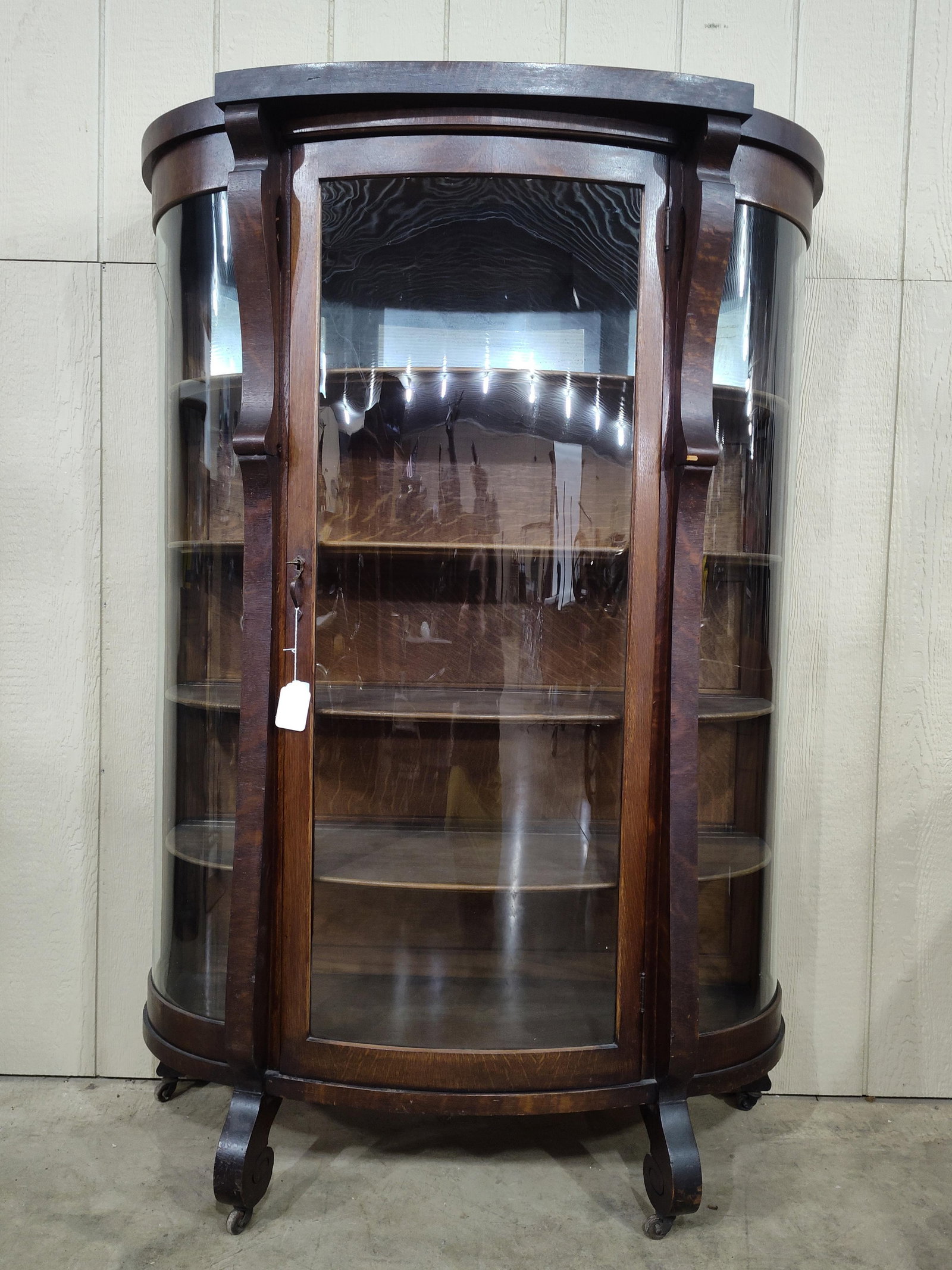 Early Quartersawn Oak Curved Front Curio Cabinet: Shows a small chip in veneer on right front pillars. Sets on casters. 43in wide 18in deep 66in tall.
