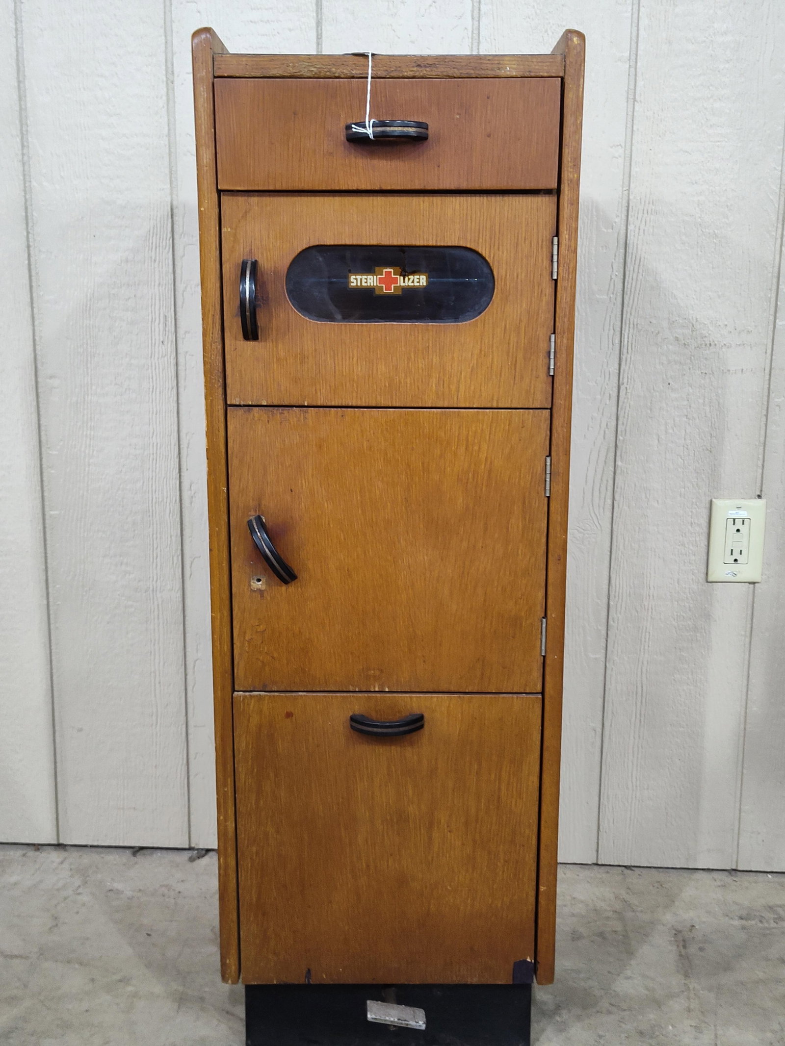 Mid Century Dental/Barbershop Sterilizer Cabinet: Wooden cabinet with a drawer on top Sterilizer and storage compartments and tilt out galvanized waste can with foot pedal. 14in wide 12in deep 42.5in tall.