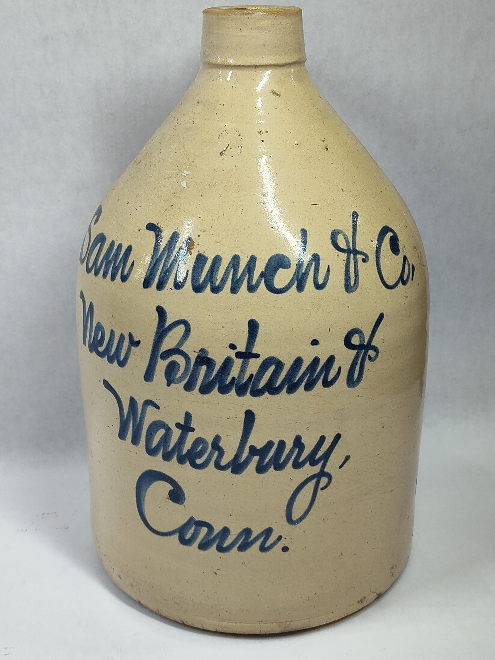 Sam Munch & Co 2-gal stoneware jug: New Britain & Waterbury, Conn. Shows a hairline in back and base. 14.5in tall.