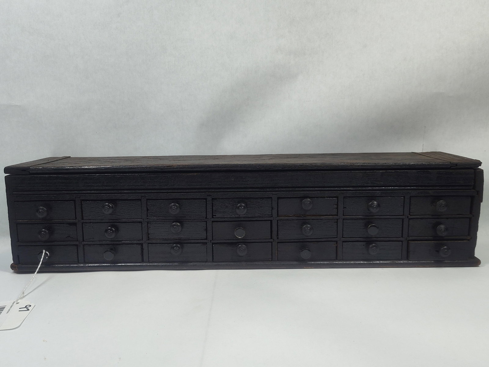 Late 1800s 21-drw Watchmakers Cabinet: 21 small drawers with storage on top under hinged Lift Top lid. Has a few replaced knobs and right side panel shows a few repairs. 23.5in long 5.25in deep 5.5in tall.