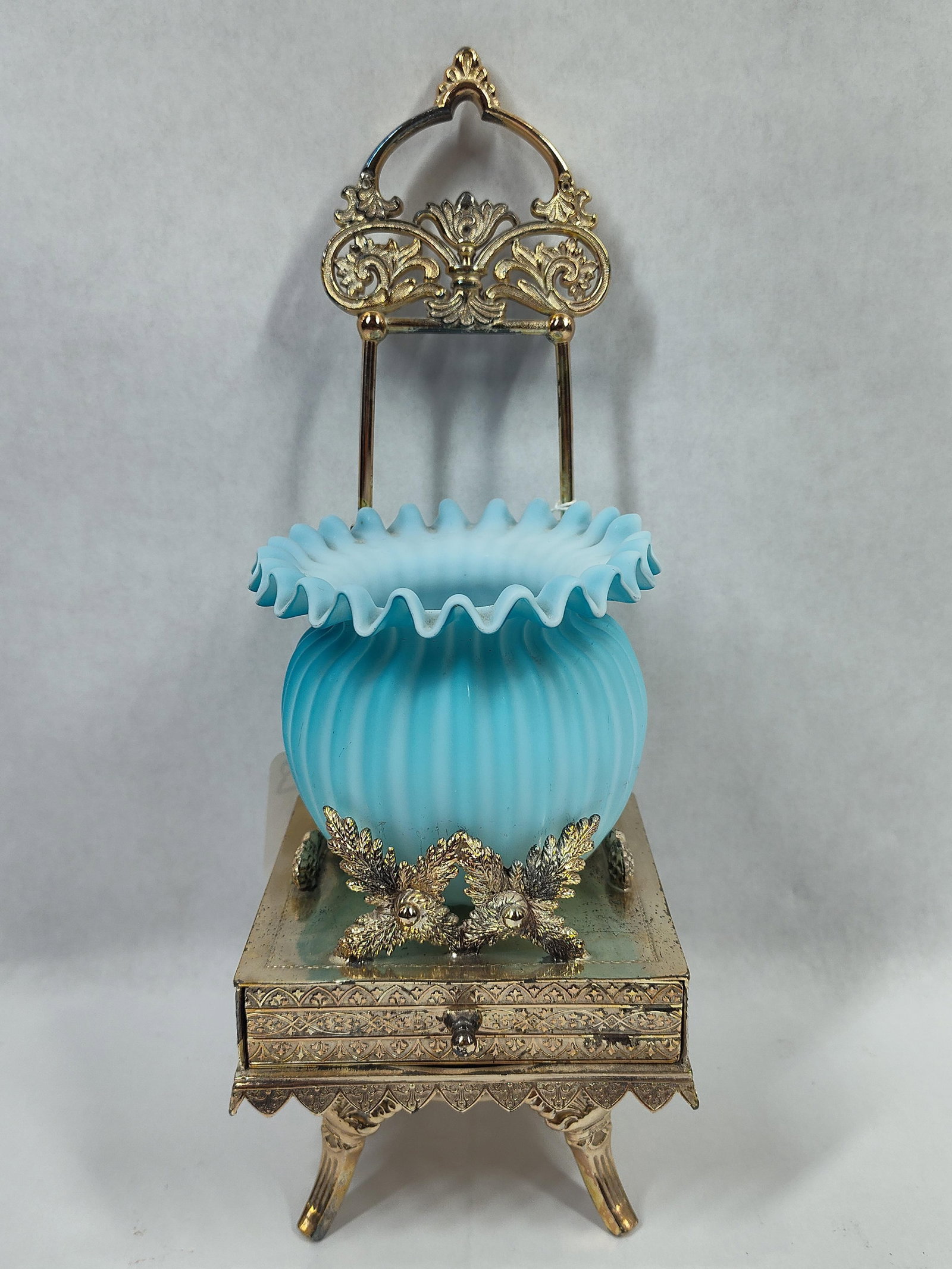 Aurora Silver Plated Sinasan: A small ornate platform featuring 4 legs and drawer. Dated between 1869-1875 by the maker mark on bottom. A rear arch with decorative detail and ornate legs, trim work, and sides. A baby blue Fenton